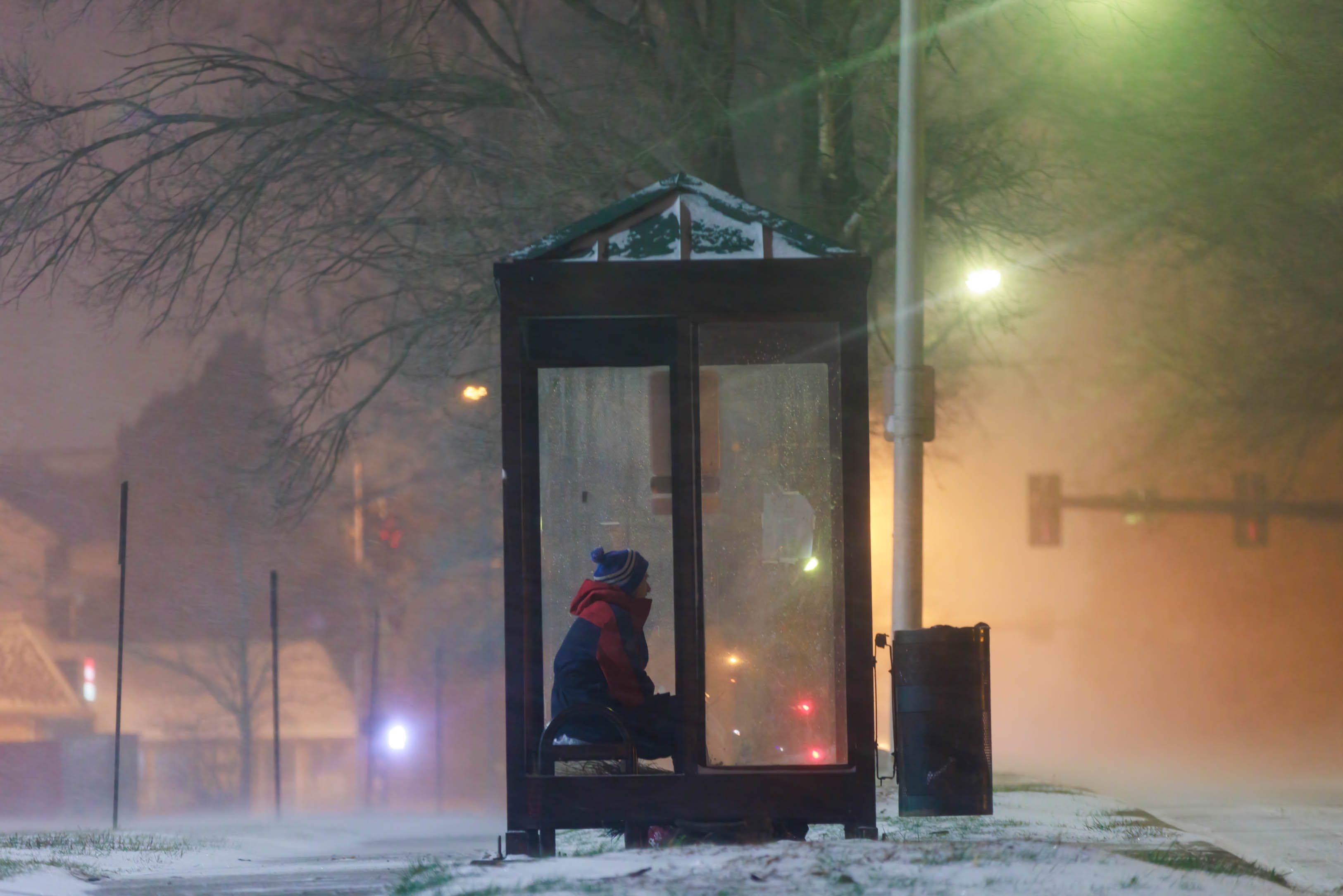 A person sits in a bus shelter during a winter storm in