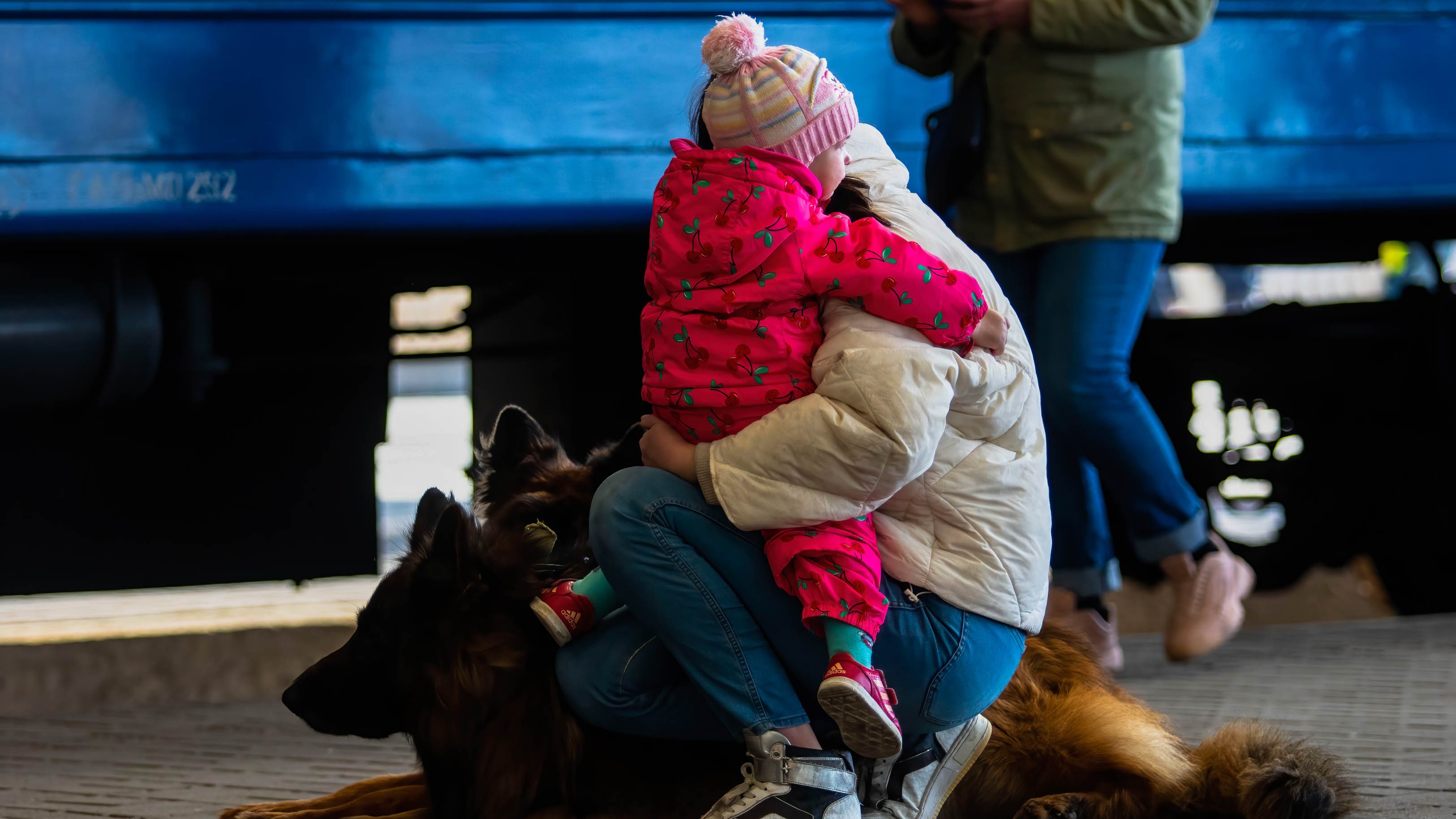 A woman holds a child and dogs on a train platform after