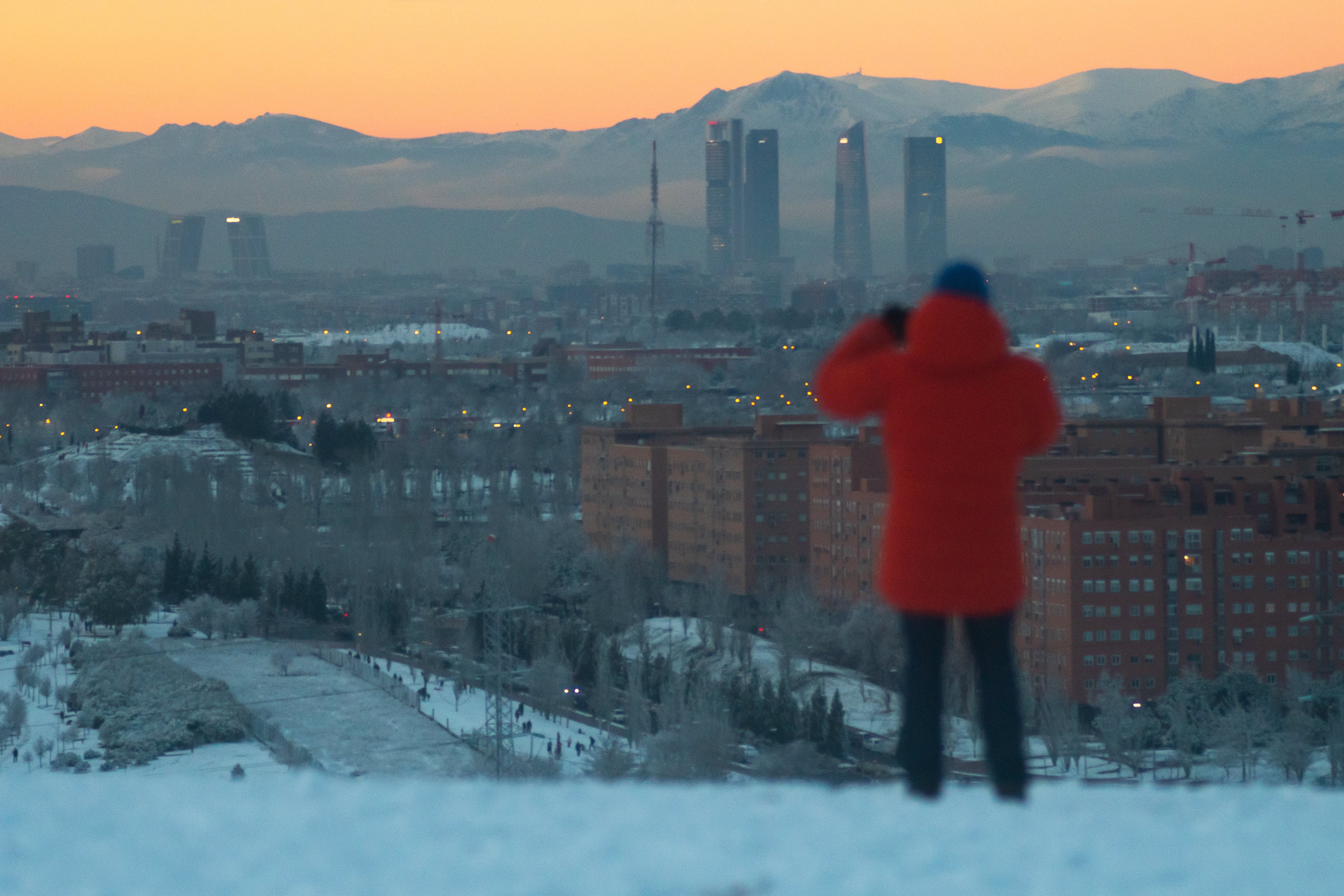A man takes pictures to Madrid skyline during a snowy day. A