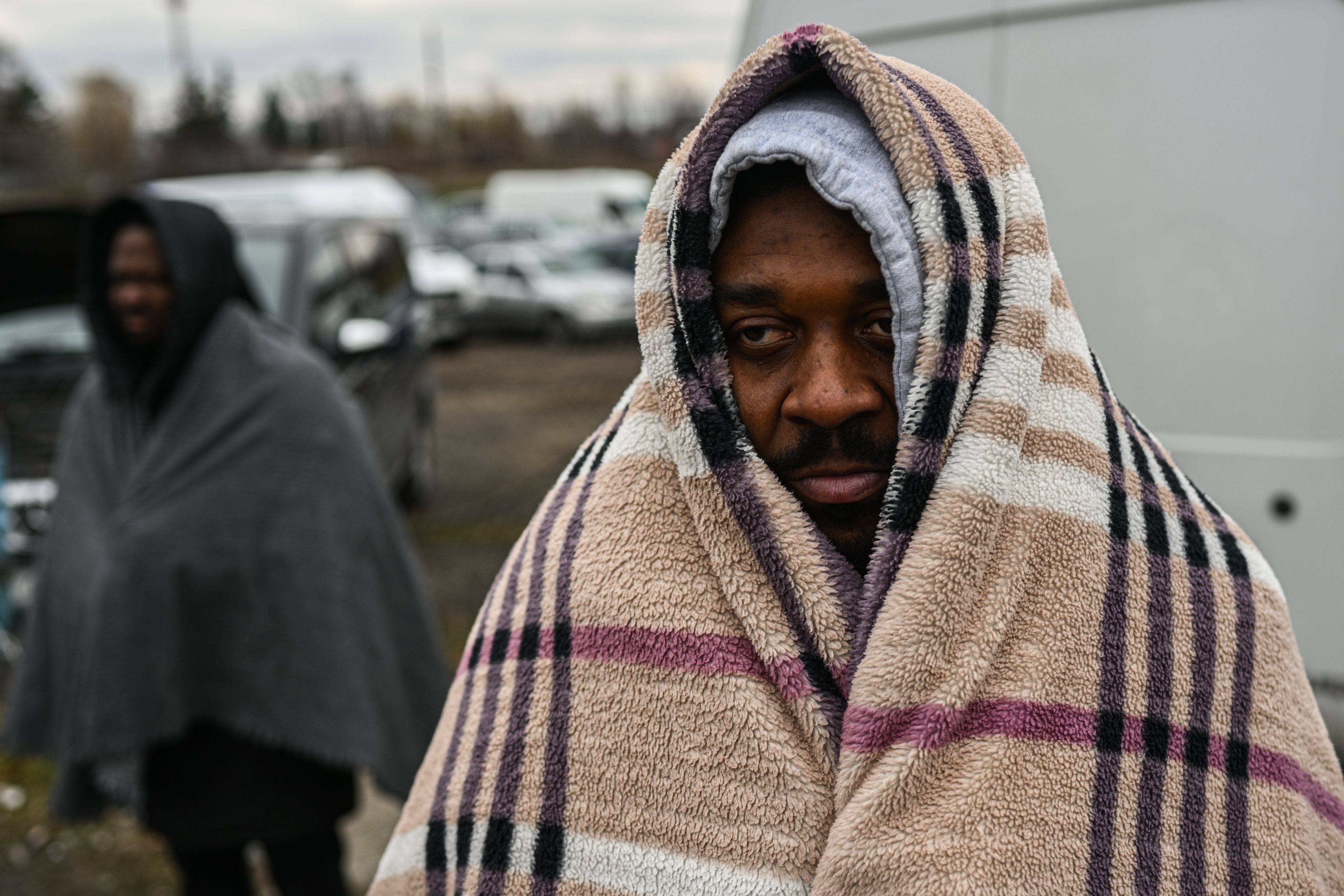 Um refugiado com uma manta para se proteger do frio aguarda por passagem na fronteira polaca