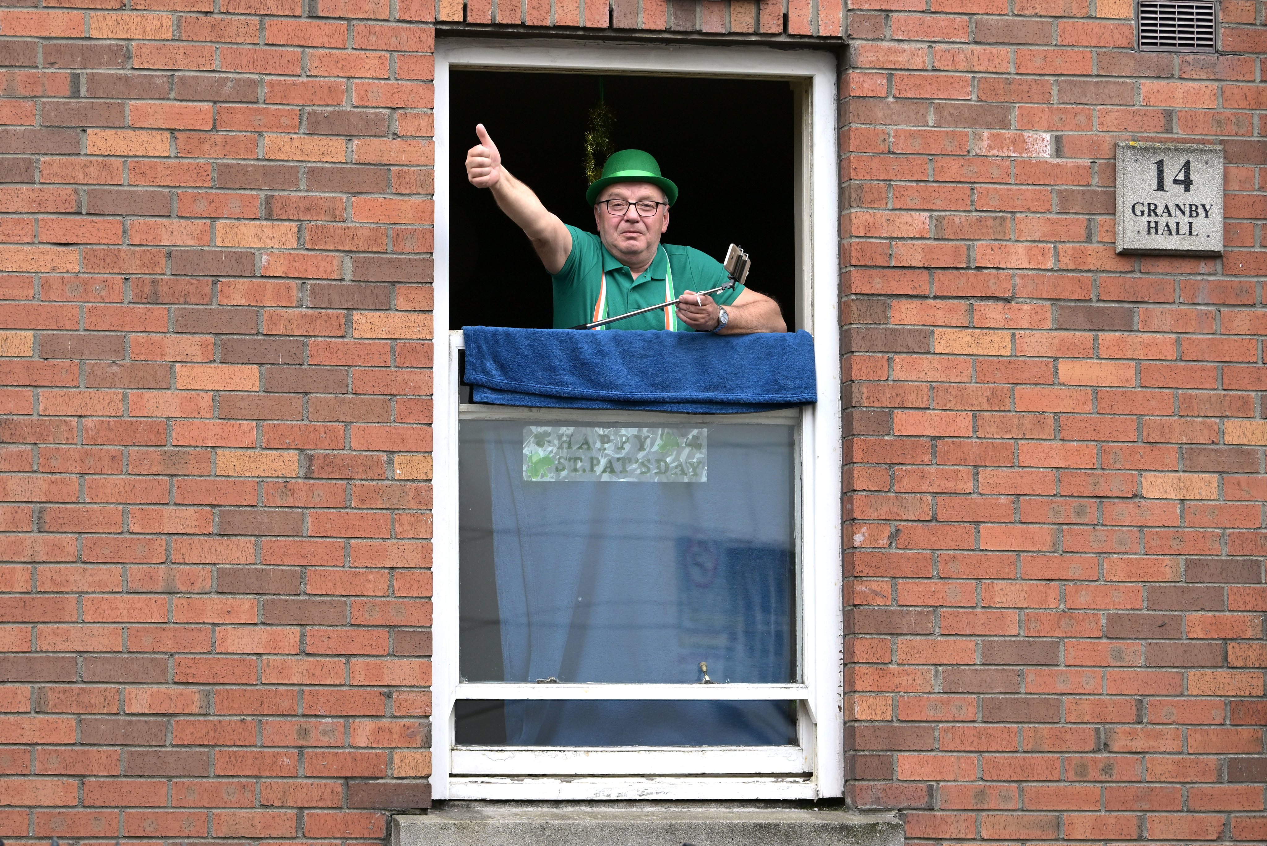 Um homem celebra o Dia de São Patrício na janela de sua casa, em Dublin