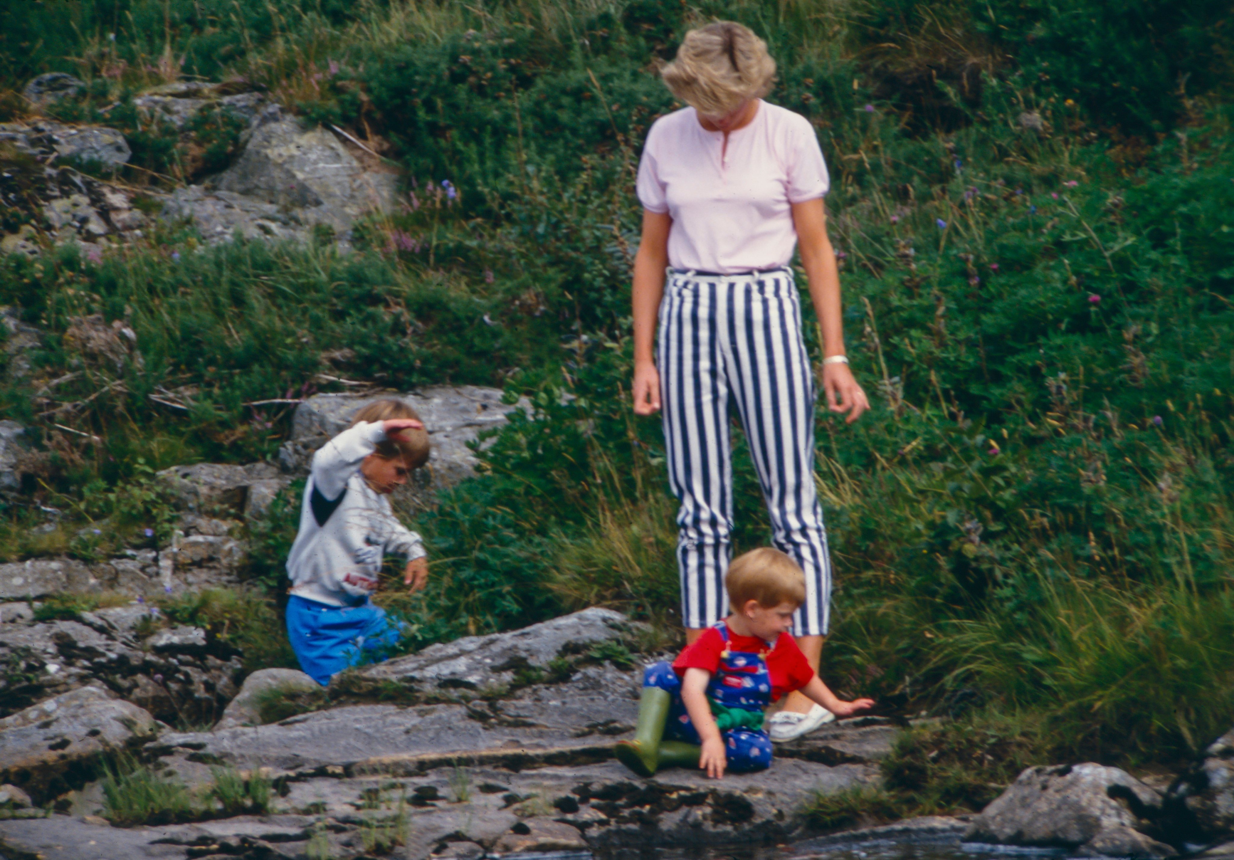 Diana, Princess of Wales, Prince William, and Prince Harry play on the banks of the River Dee, near Balmoral Castle