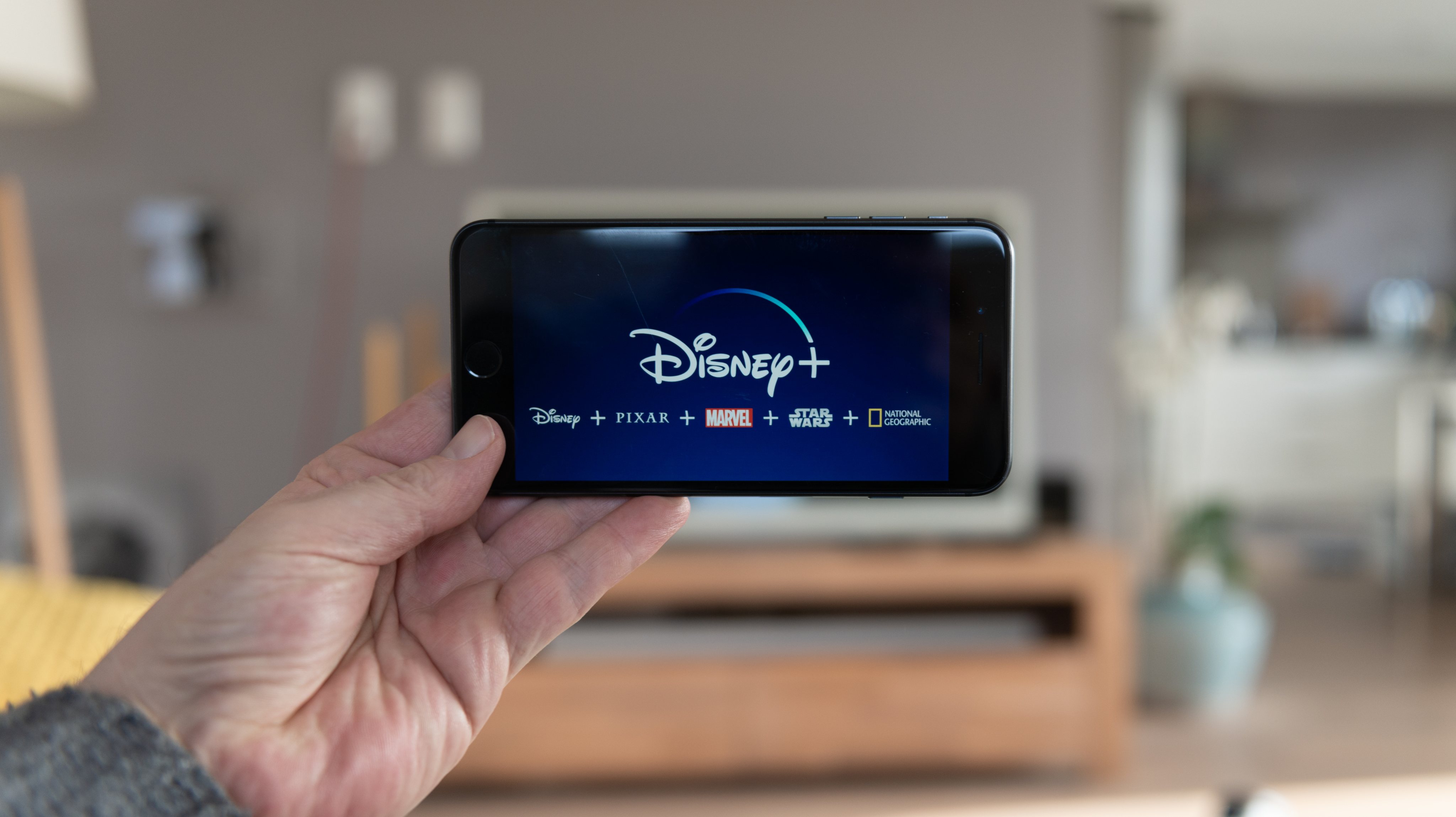 Disney+ startscreen on  mobile phone. Disney+ online video, content streaming subscription service. Man holds his smartphone up and looks at disney plus
