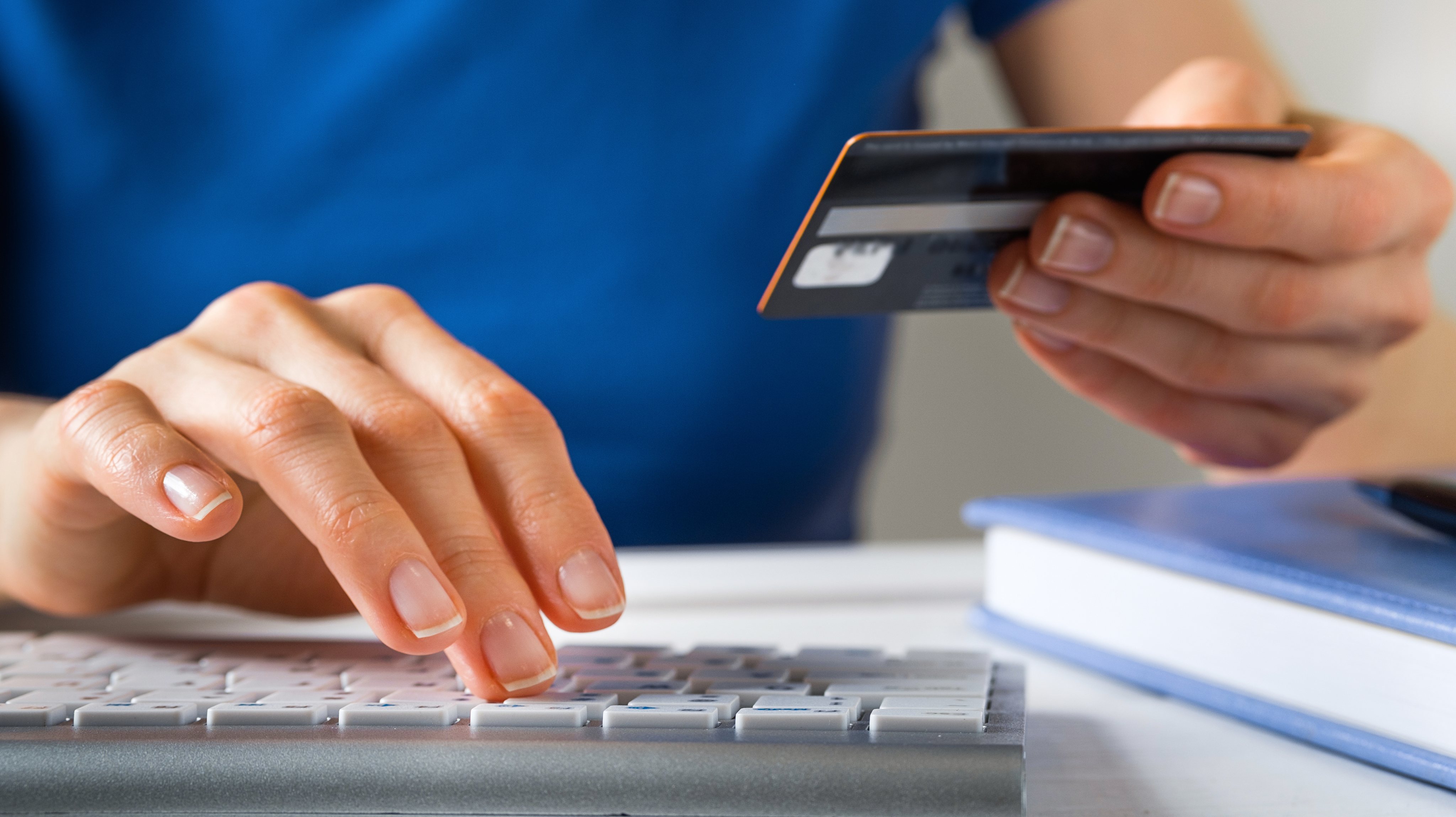 A Woman Is Holding A Credit Card, Typing on A Laptop Keyboard. There&#039;s a Notepad and a Pen next to it. The Concept of Buying Online, Ordering Products at Home, and paying via the Internet.