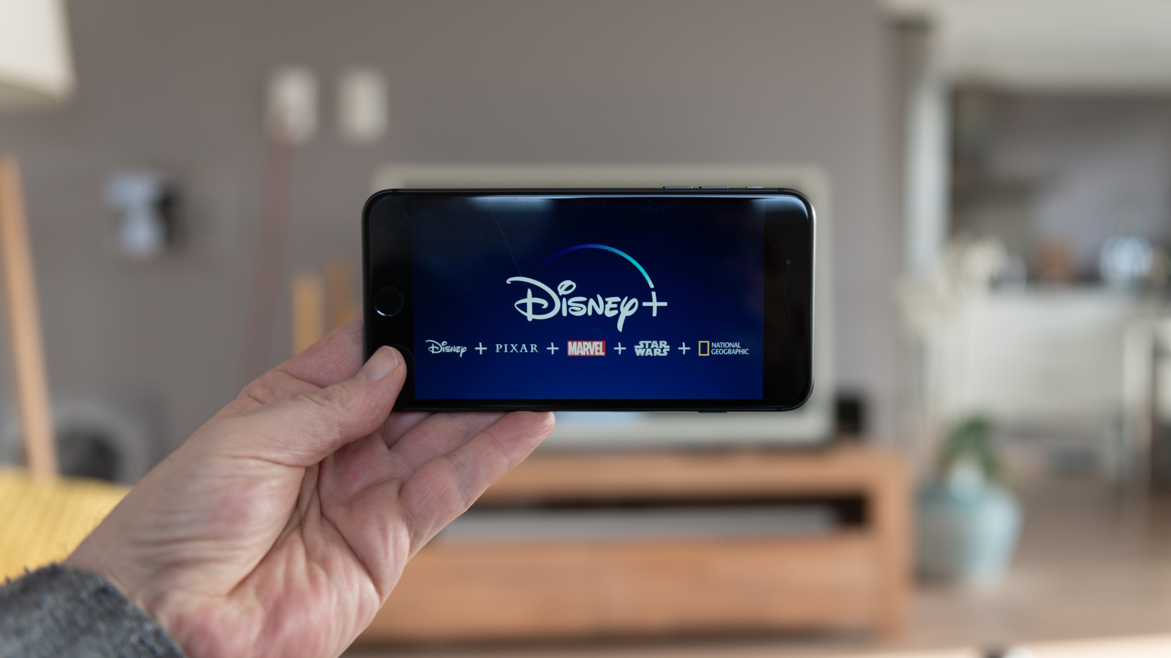 Disney+ startscreen on  mobile phone. Disney+ online video, content streaming subscription service. Man holds his smartphone up and looks at disney plus