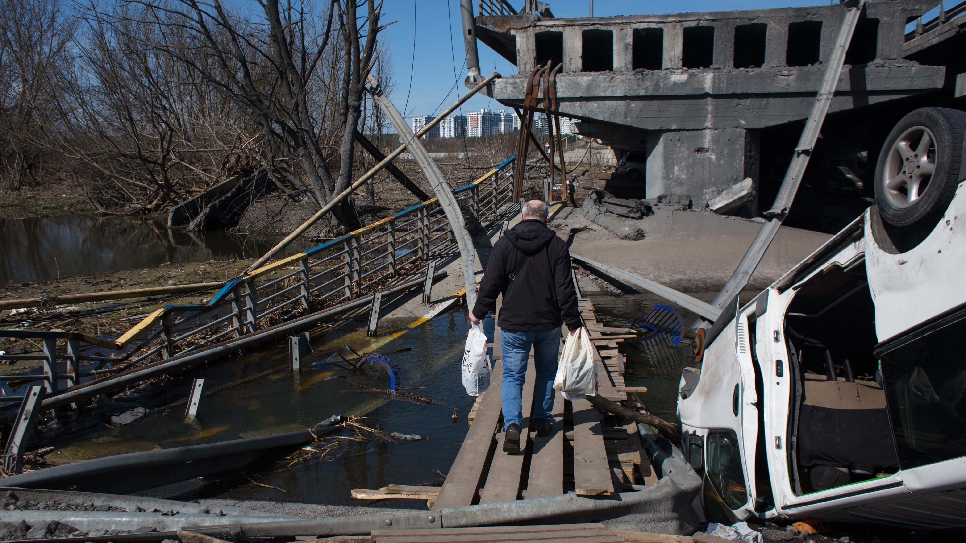Um homem atravessa com as compras os destroços de uma ponte destruída em Irpin, na Ucrânia