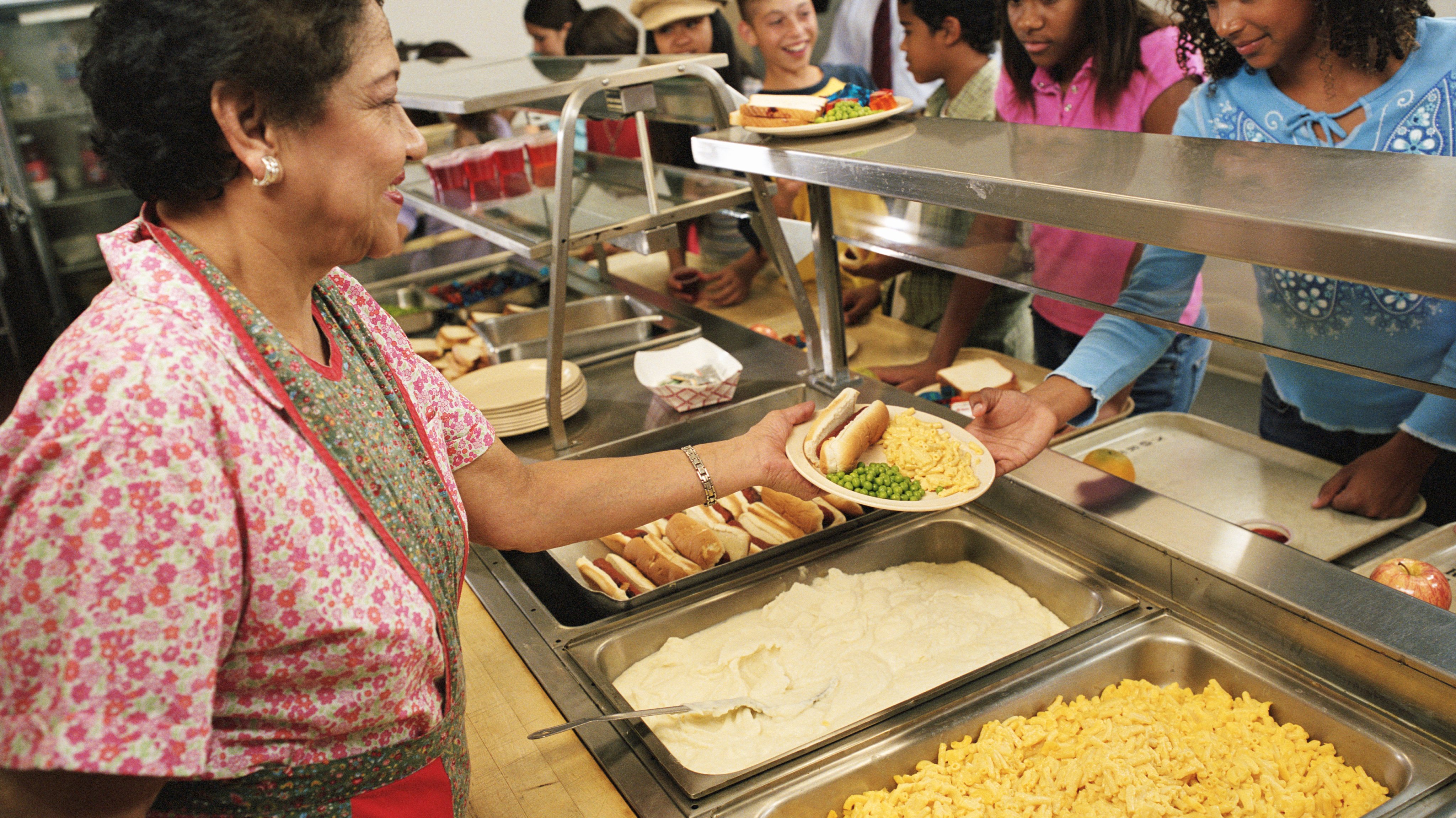 Mature woman serving food to students (12-14) in cafeteria