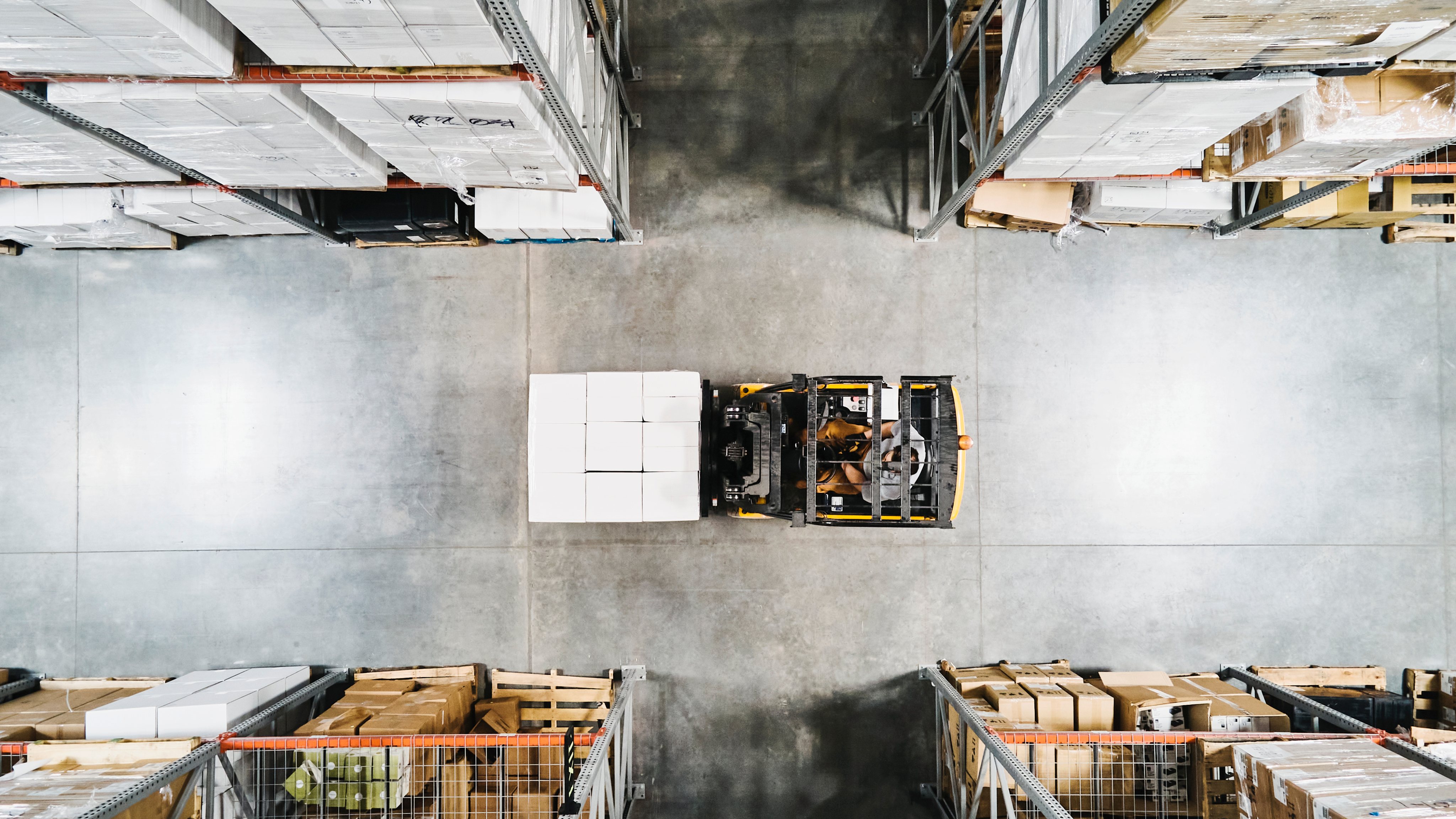 Overhead view of warehouse worker moving pallet of goods with forklift in warehouse