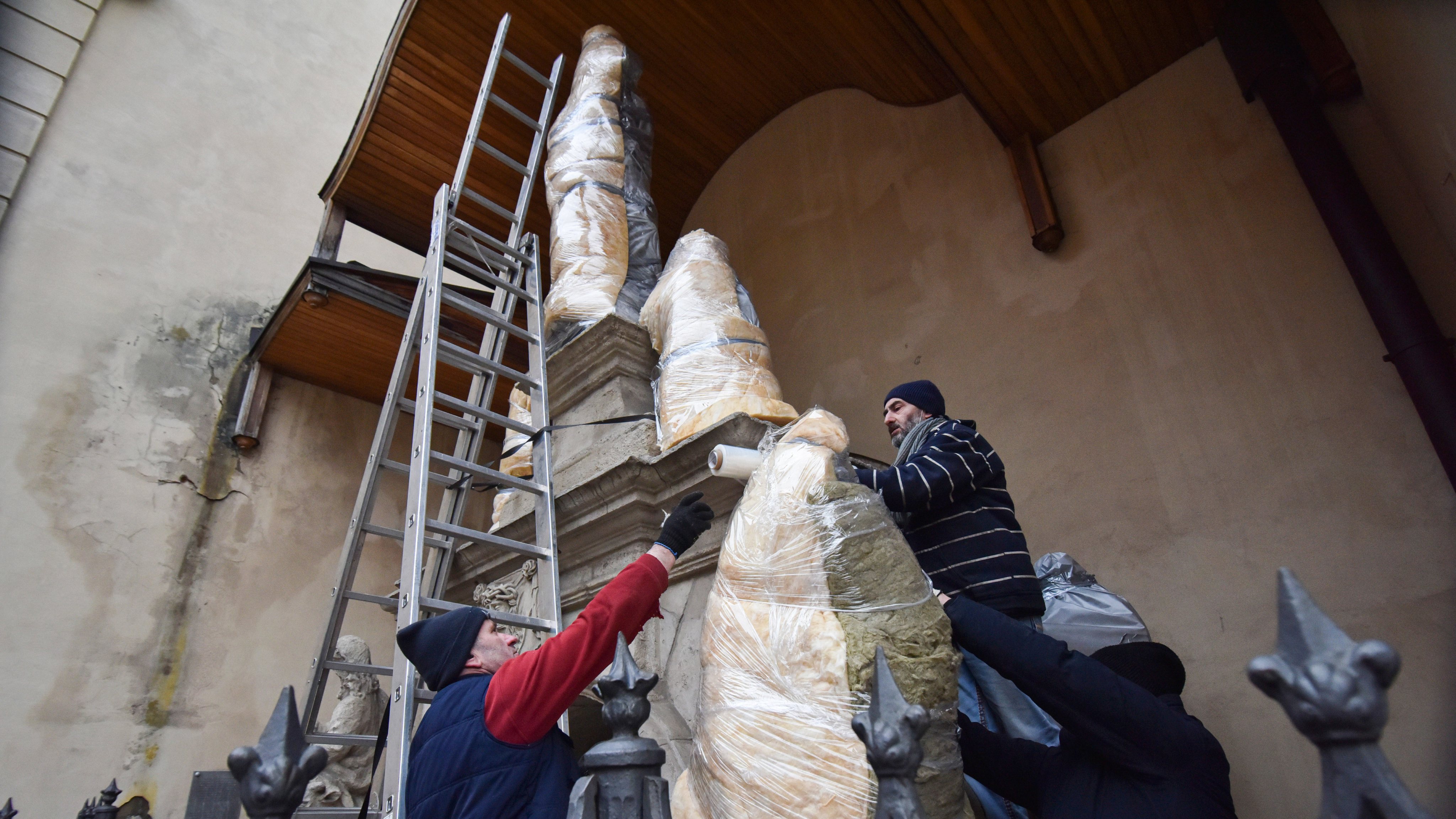 Workers wrap sculptures near Latin Cathedral in Lviv to