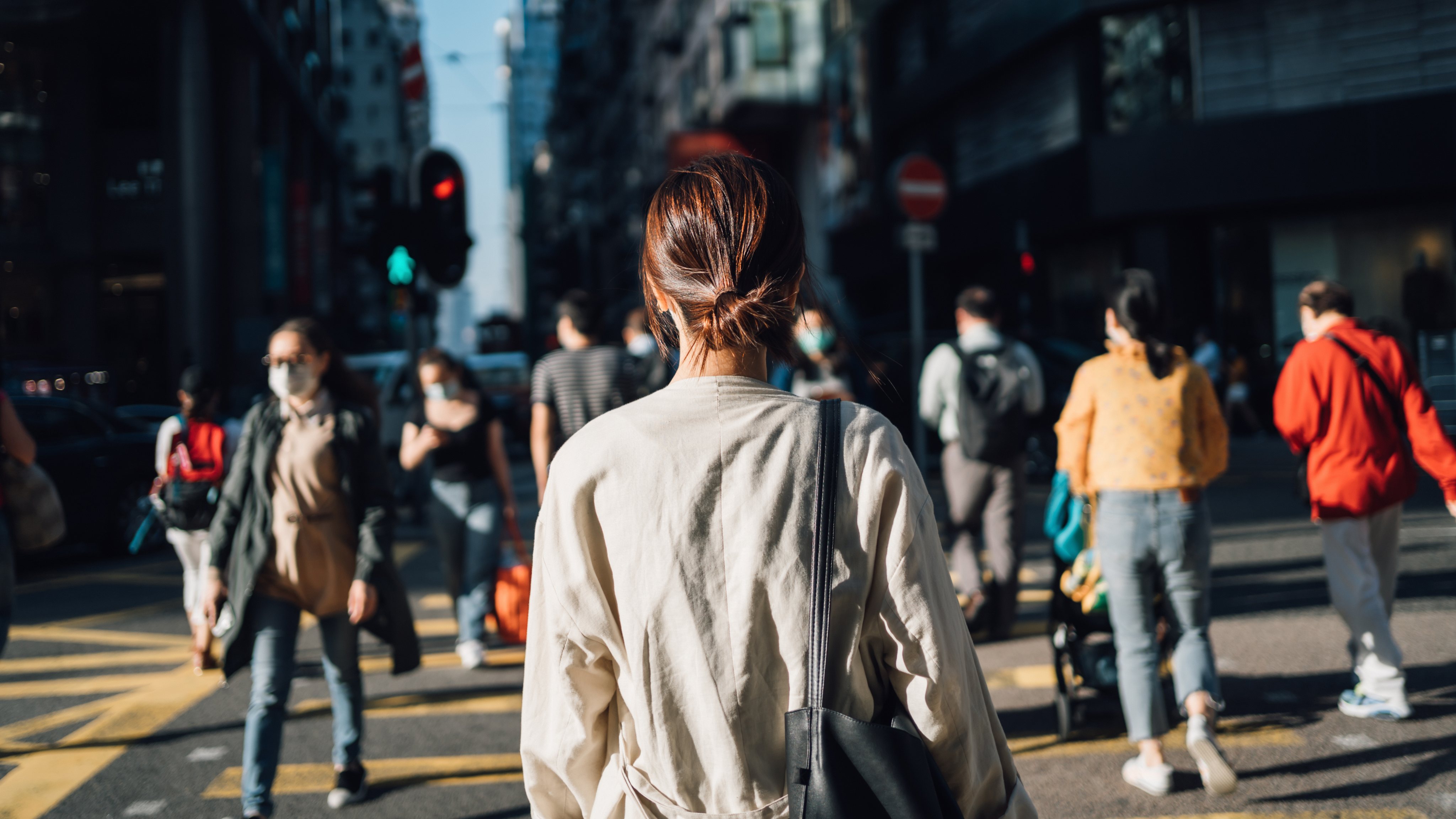 Rear view of young Asian woman commuting to work in city in the fresh morning, crossing street amidst crowd of pedestrians. Daily life and routine of a businesswoman