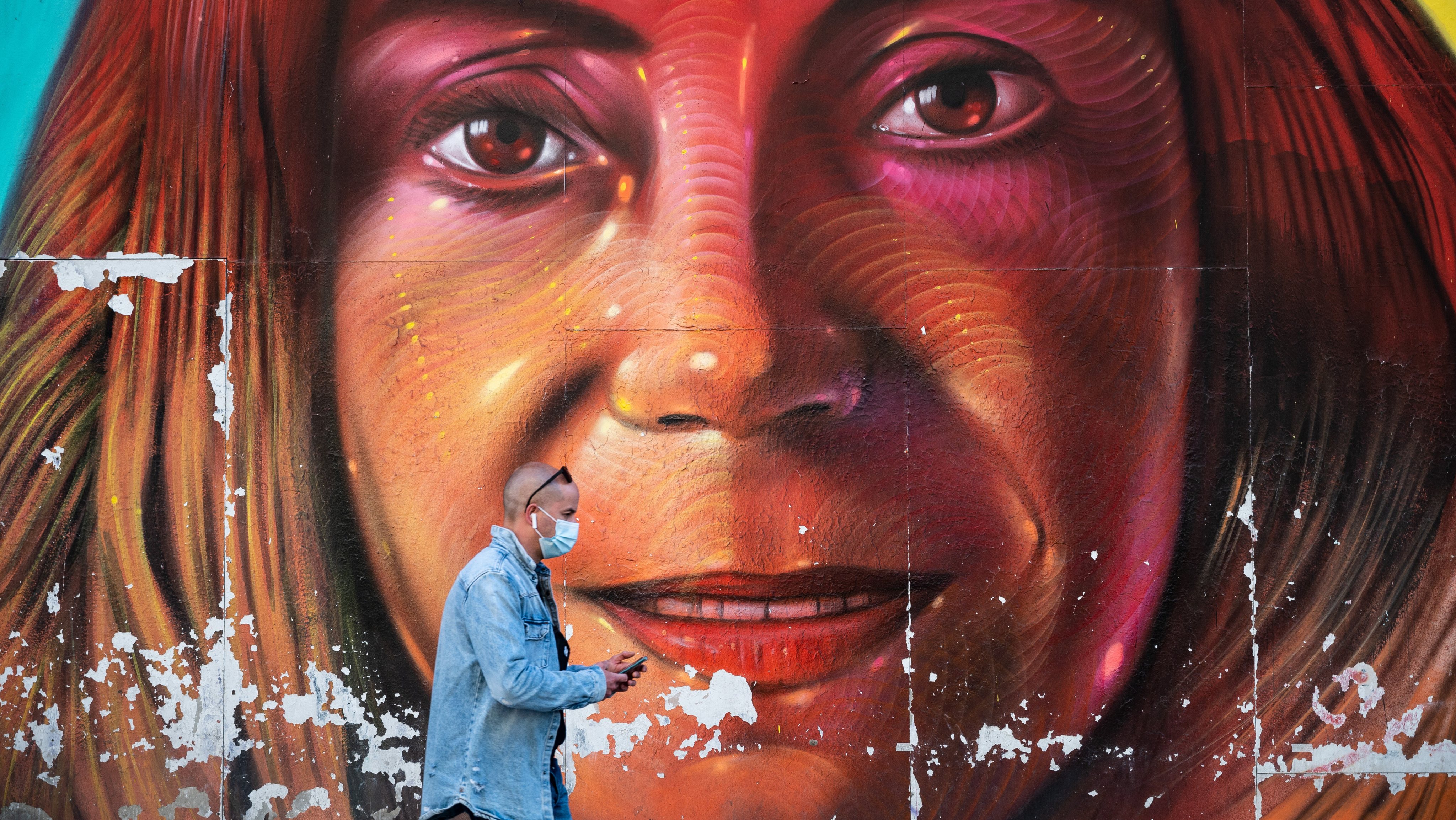 A man walks past a mural in Gran Via street wearing a face