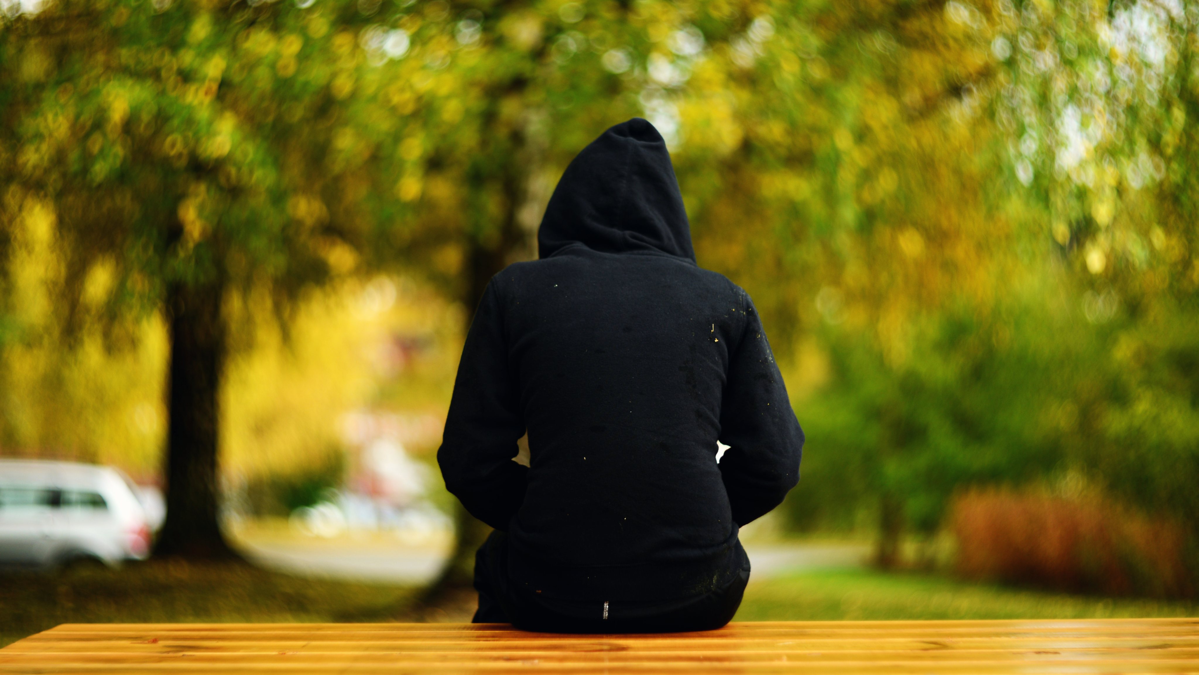 a girl in black hooded shirt with hoodie on her head sitting on a bench