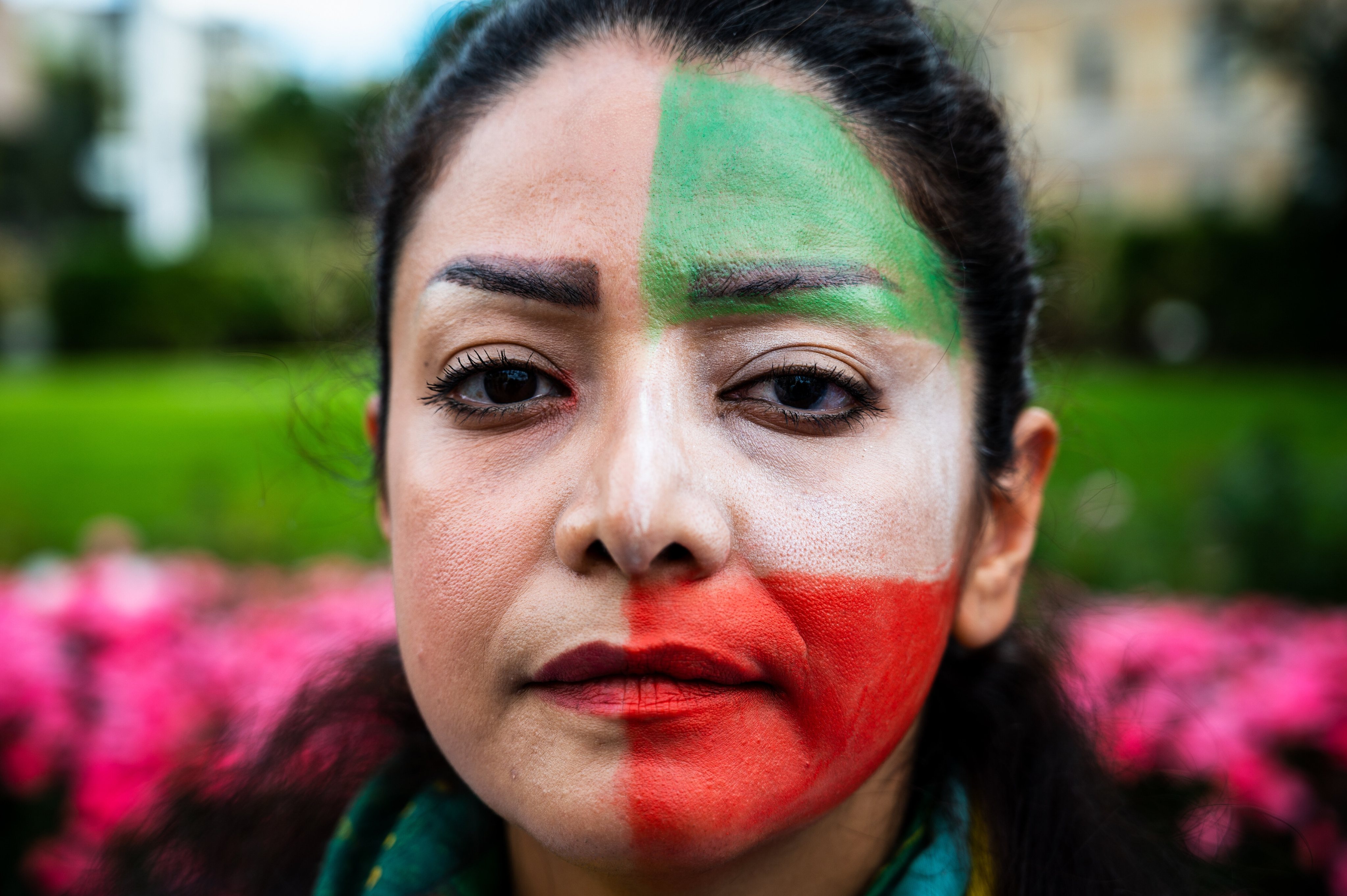 A woman with the flag of Iran painted on her face posing for