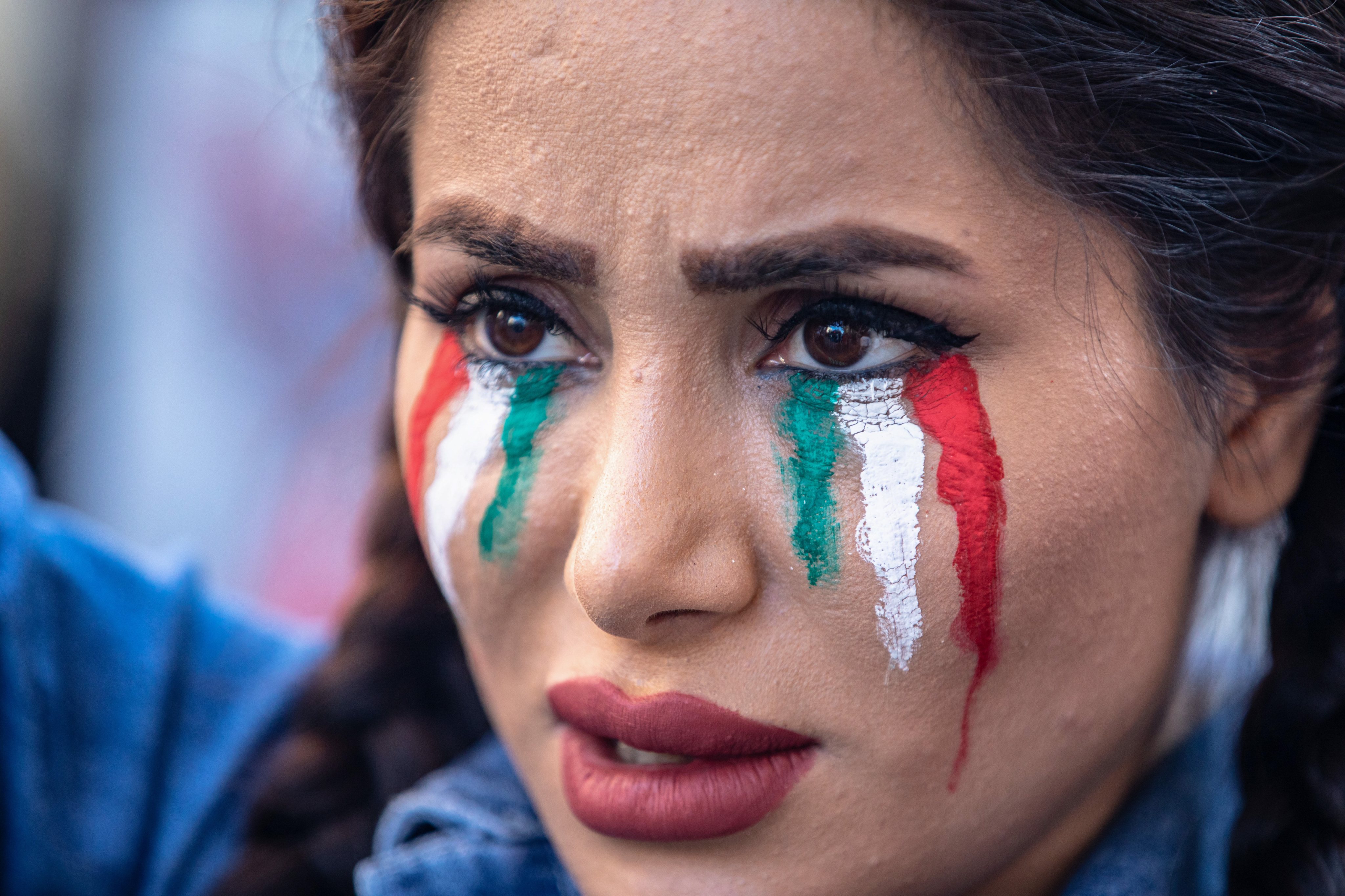 A protester with paintings of Iranian flag on her face takes