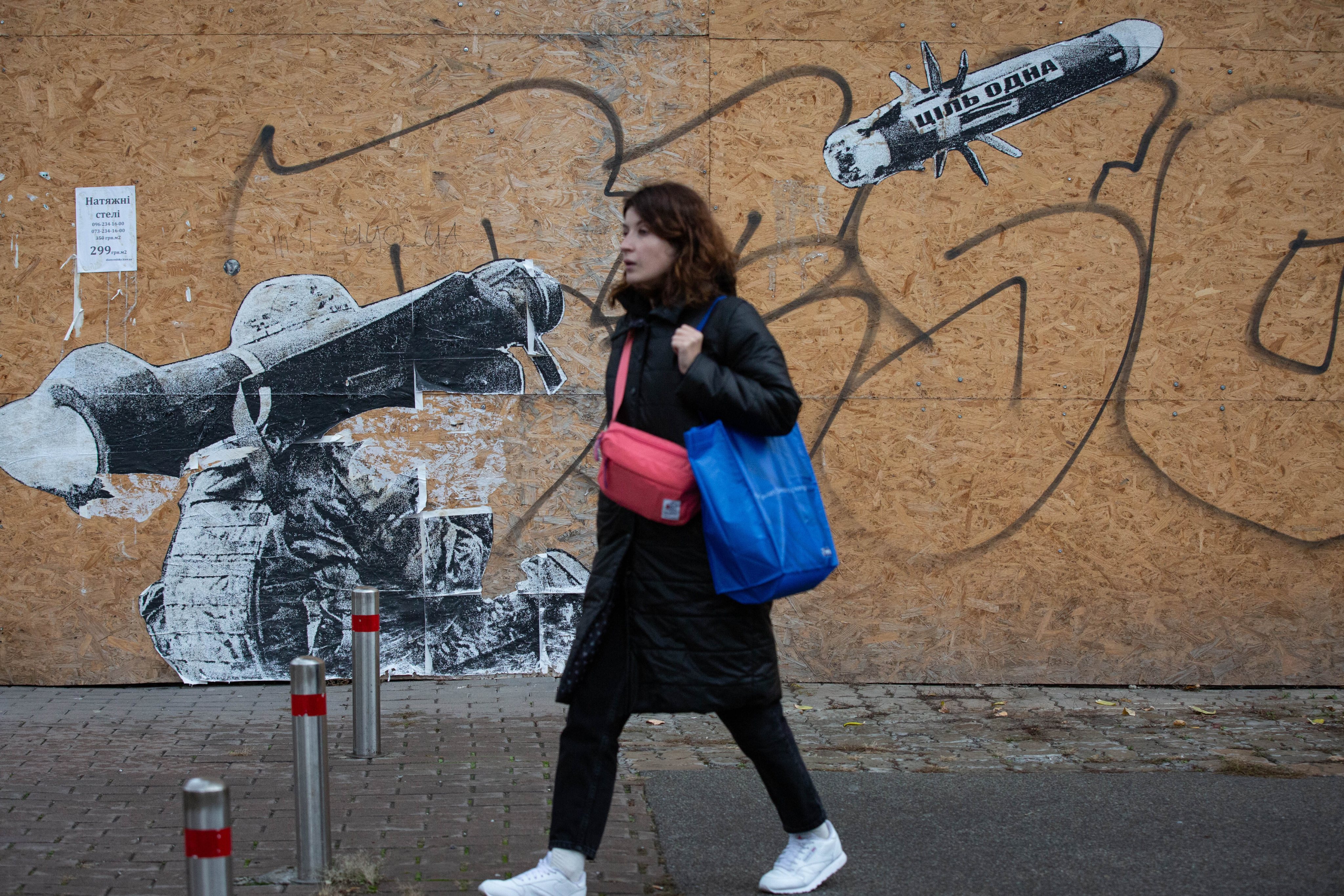 A girl passes by graffiti depicting a Ukrainian serviceman