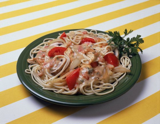 A dish of Italian-style pasta noodles with a chicken, onion, mushroom, and tomato sauce, and parsley, sits on a yellow and white striped surface, 1970s. (Photo by Hulton Archive/Getty Images)