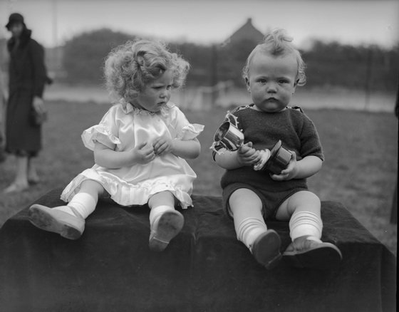 8th May 1934:  Twins Michael and Mary Kerby fail to convey any enthusiasm upon winning a trophy in a Baby Show at Ruislip, Middlesex.  (Photo by Martin/Fox Photos/Getty Images)