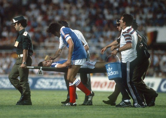SEVILLA, SPAIN - JULY 8:  French defender Patrick Battiston is carried off the field on a stretcher as captain Michel Platini tries to comfort him during the World Cup semifinal soccer match between West Germany and France. Battiston collided with West German goalkeeper as he was going for the ball.  AFP PHOTO  (Photo credit should read STAFF/AFP/Getty Images)