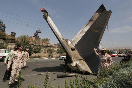 A member of the Iranian Revolutionary Guards reacts as he stands next to the remains of a plane that crashed near Tehran's Mehrabad airport on August 10, 2014. A civilian airliner crashed on take-off near the Mehrabad airport in the capital, Iranian news agencies said, with reports that almost 50 people were killed. AFP PHOTO / ATTA KENARE        (Photo credit should read ATTA KENARE/AFP/Getty Images)