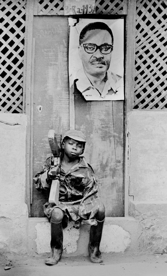 HUAMBO, ANGOLA:  A young soldier of the Popular Movement for the Liberation of Angola (MPLA) is seated on a doorstep 23 February 1976 in Huambo. Over his heads hangs the portrait of his leader Agostinho Neto. Former Portuguese colony, the Republic of Angola went to a civil war after its independence in1975, with three infernal factions, the Marxists MPLA, UNITA (The National Union for the Total Independence of Angola) and the FLNA (National Front for the Liberation of Angola).  Un jeune soldat du Mouvement Populaire de LibTration de l'Angola (MPLA) est assis sur le pas d'une porte le 23 fTvrier 1976 a Huambo. Au dessus de lui, est accrochT un portrait de son leader Agostinho Neto. Ancienne colonie portugaise, la RTpublique d'Angola connait aprFs son indTpendance en 1975 une guerre civile opposant trois factions, les marxistes MPLA, l'UNITA (Union National pour l'IndTpendance Totale de l'Angola) et le FLNA (Front National de LibTration de l'Angola). (Photo credit should read AFP/Getty Images)