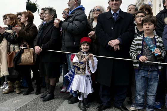 A boy dressed in Greek traditional costume holds a Greek flag, as he watches the student parade on the eve of Greece's Independence day, commemorating the 1821 start of the war against the Ottoman rule on March 24, 2015.  AFP PHOTO/ LOUISA GOULIAMAKI        (Photo credit should read LOUISA GOULIAMAKI/AFP/Getty Images)