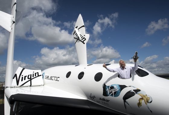 British billionaire Richard Branson poses for photographs in the window of a replica of the Virgin Galactic, the world?s first commercial spaceline, at the Farnborough International Airshow in Hampshire, southern England, on July 11, 2012. Virgin Galactic announced ?LauncherOne,? a new air-launched rocket specifically designed to deliver small satellites into orbit. Commercial flights of the new orbital launch vehicle are expected to begin by 2016, Virgin Galactic aims to offer frequent and dedicated launches at the world?s lowest prices. AFP PHOTO / ADRIAN DENNIS        (Photo credit should read ADRIAN DENNIS/AFP/GettyImages)