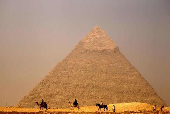 Egyptians ride their camels past the pyramid of Khafre (Chefren) in Giza, on the outskirts of Cairo, on November 30, 2010. AFP PHOTO/PATRICK BAZ (Photo credit should read PATRICK BAZ/AFP/Getty Images)