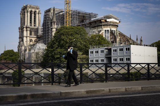 epa08358419 A man wearing protective gloves and a face mask walks past Notre-Dame Cathedral on Easter Sunday, in Paris, France, 12 April 2020. Easter and religious celebrations are held behind closed doors as France is under lockdown in an attempt to stop the widespread of the SARS-CoV-2 coronavirus causing the Covid-19 disease.  EPA/IAN LANGSDON