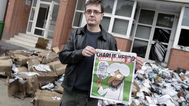 Charb (na foto) em frente à sede do jornal que, em 2011, ficou destruída depois de um ataque de uma bomba incendiária