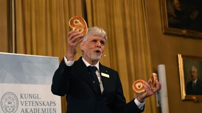 Thors Hans Hansson, membro do Comité do Nobel para a Física usou um pretzel (dois buracos), um bagel (um buraco) e um bun (sem buraco) para apresentar o trabalho dos laureados