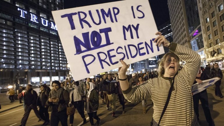 Protesto em Chicago, com manifestante a mostrar cartaz que diz: &quot;Trump não é o meu presidente&quot;