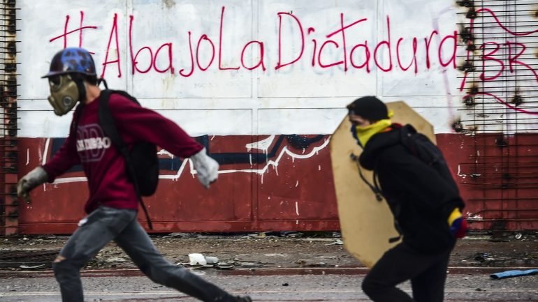 Dois manifestantes contra Nicolás Maduro fogem das investidas da Guarda, em Caracas, durante os protestos de domingo, 30 de julho