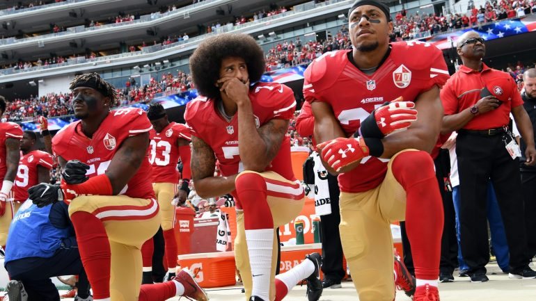 Eli Harold, Colin Kaepernick e Eric Reid dos San Francisco 49ers, de joelhos durante o hino nacional em protesto contra a discriminação racial