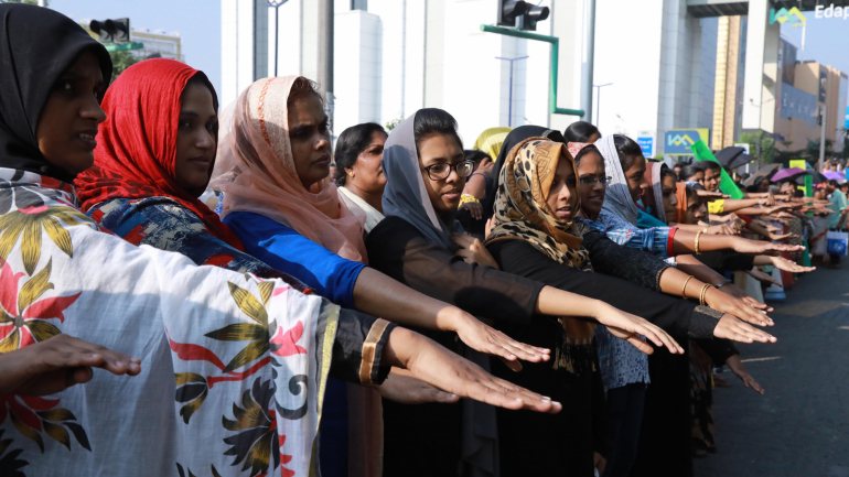 Mulheres indianas erguem as mãos enquanto formam um cordão humano para combater a discriminação de género