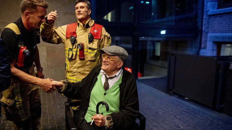 David Hockney sorridente ao lado dos bombeiros que o resgataram depois de ter ficado preso num elevador