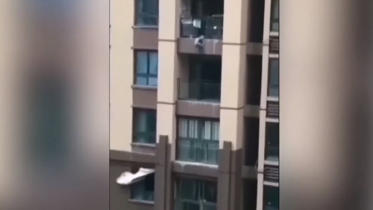 As imagens em vídeo mostram a criança pendurada de uma varanda do prédio