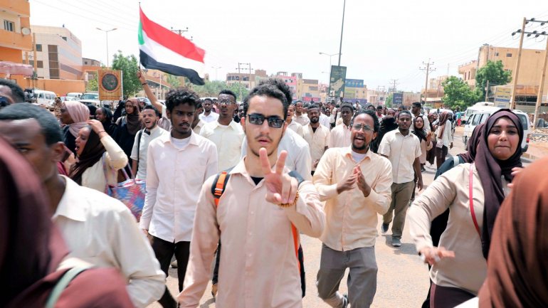 Uma multidão reuniu-se à porta da sala de negociações em Cartum, agitando bandeiras sudanesas e gritando &quot;civis, civis&quot;