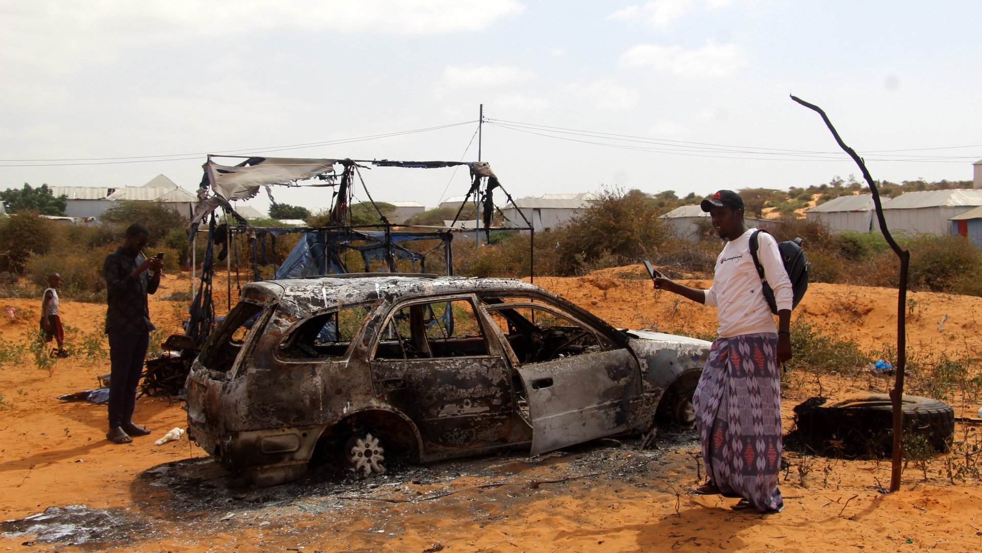 Pessoas perto dos destroços de um carro após um ataque à esquadra da polícia em Kaxda, na Somália. 16 de fevereiro de 2022