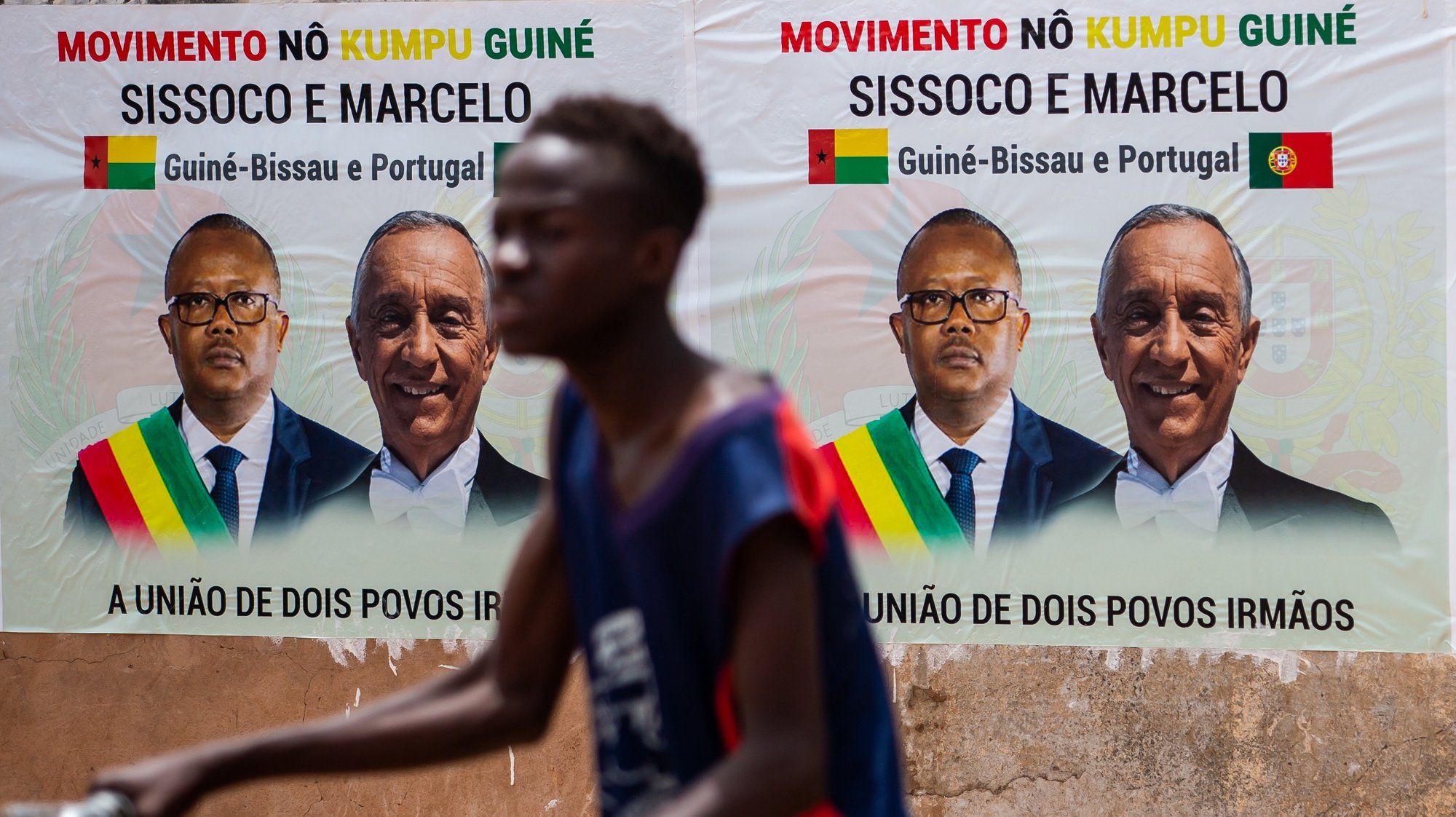 Um homem passa por um cartaz com a  informação da visita oficial do Presidente da República, Marcelo Rebelo de Sousa, que decorre entre 17 e 18 de maio em Bissau, na Guiné-Bissau, 17 de maio de 2021. JOSÉ SENA GOULÃO/LUSA