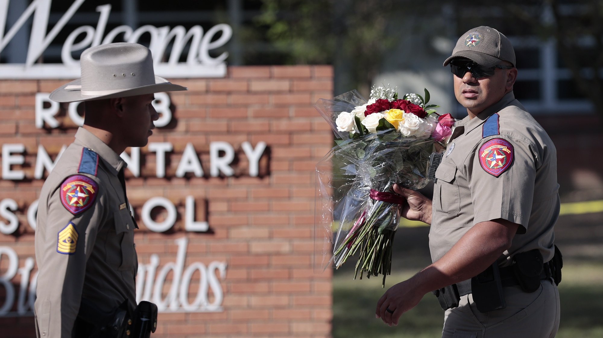 epa09974978 A Texas State Trooper carries flowers near the Robb Elementary School sign as police and investigators continue to work at the scene of a mass shooting at the school which killed 19 children and two adults according to Texas Governor Greg Abbott in Uvalde, Texas, USA, 25 May 2022. The eighteen-year-old gunman was killed by responding officers.  EPA/AARON M. SPRECHER