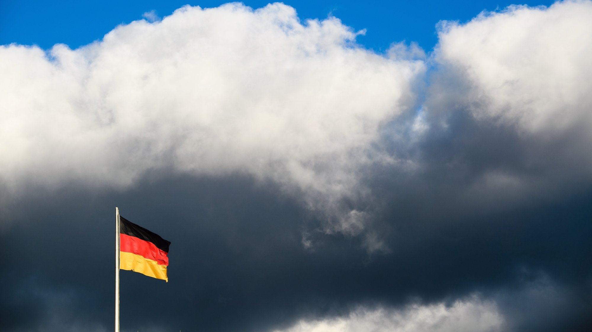 epa09078555 Clouds are seen over a German national flag at the Reichstag building, the seat of the German parliament, in Berlin, Germany, 16 March 2021.  EPA/CLEMENS BILAN