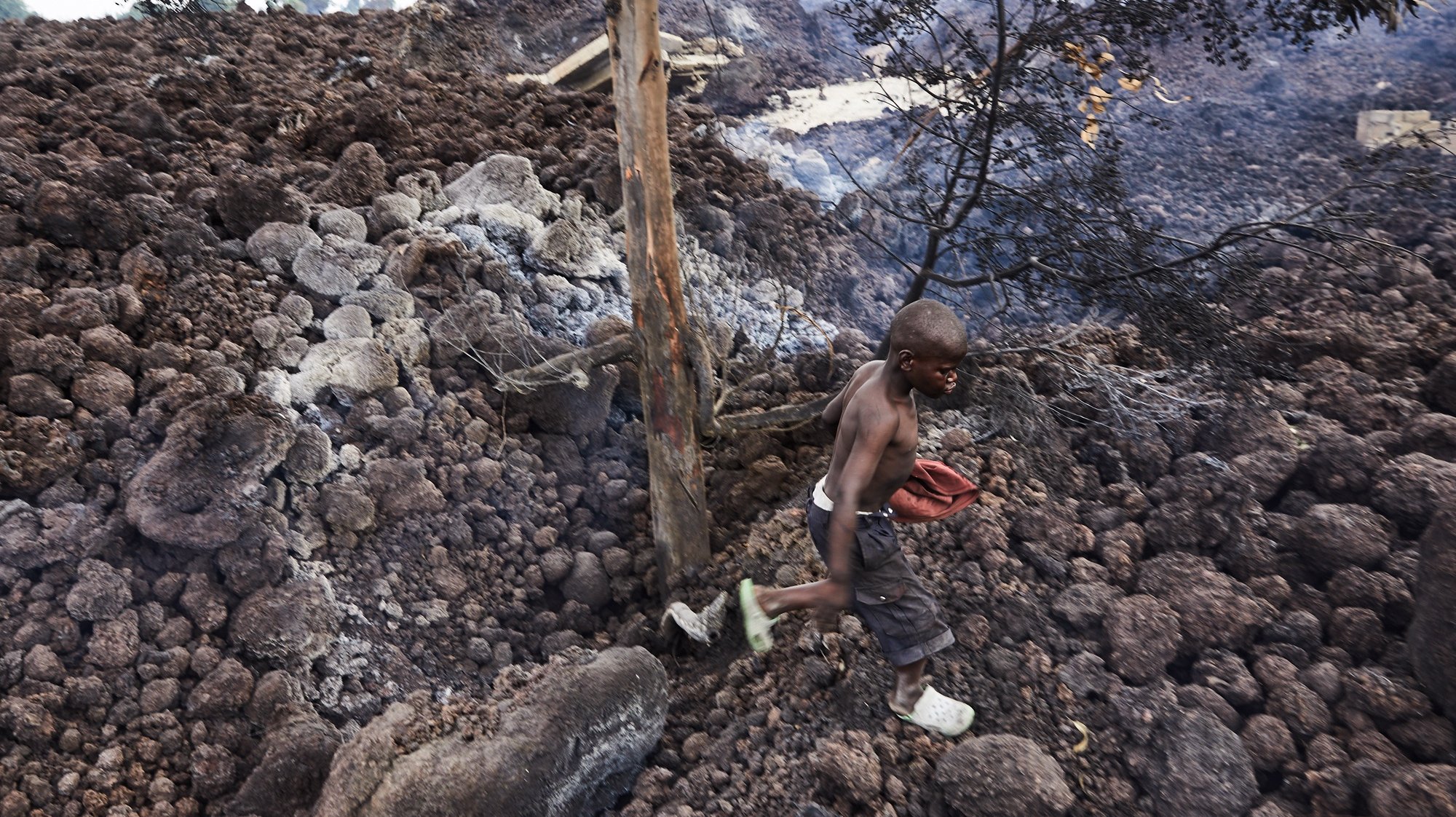 epa09227820 A Congolese boy in the neighbourhood of Buhene walks on piles of lava in the aftermath of a volcanic eruption in Goma, Democratic Republic of Congo, 25 May 2021. One of the planets most active volcanoes Mount Nyiragongo in eastern Democratic Republic of Congo erupted 22 May 2021. According to local journalists, aftershocks from the Nyiragongo volcanic eruption continue in the town of Goma. According to the United Nations children&#039;s agency (UNICEF) 25 May 2021 more than 100 children are missing after having been separated from their parents. Foreign countries, like the United Kingdom, have warned their nationals through their embassies of the continuation of seismic activity and cannot rule out further fissures or lava flow.  EPA/HUGH KINSELLA CUNNINGHAM