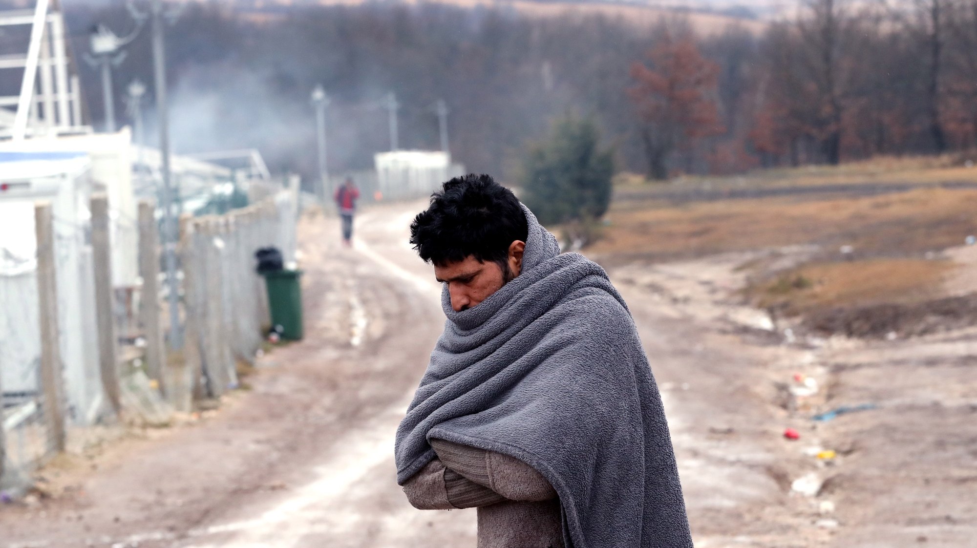 epa08914435 A migrant tries to warm himself at the Lipa camp in Bihac, Bosnia and Herzegovina, 01 January 2021. Some thousand refugees at the camp were scheduled to be relocated from the burnt-down tent camp on 31 December, yet were returned to Lipa camp. A fire on 23 December destroyed most of the camp near the city of Bihac, which has already been sharply criticized by international authorities and aid groups as unsuitable for accommodating refugees and migrants.  EPA/FEHIM DEMIR
