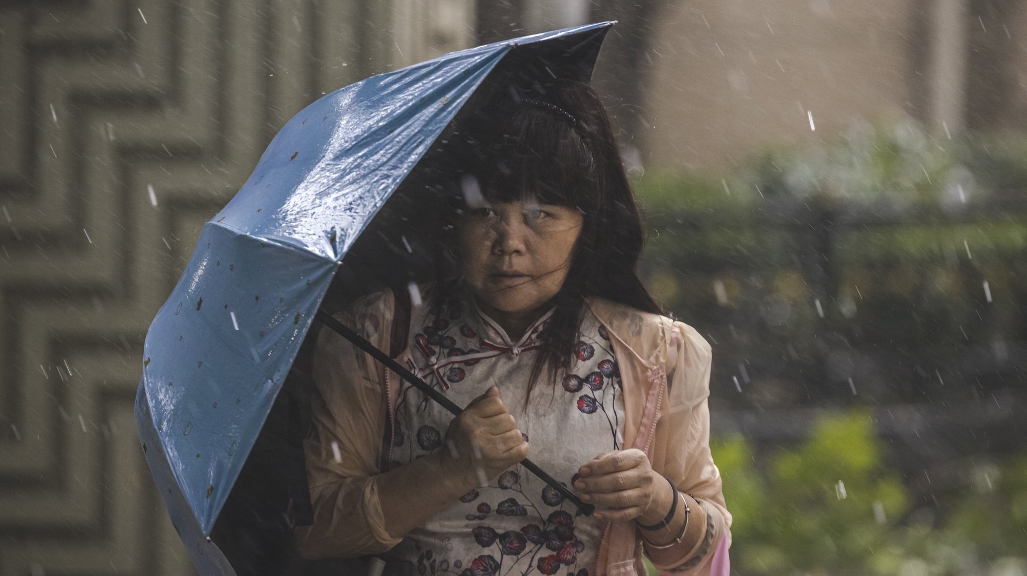 epa09364992 A woman walks on the street during the heavy winds and rain caused by “In-Fa” typhoon in Shanghai, China, 25 July 2021. After the typhoon Cempaka hit South China on 20 July and heavy rain in Central China causing flooding on 21 July, Shanghai braces for the typhoon In-Fa. According to a China Meteorological Administration report, In-Fa landed 25 July, at 12:30 pm local time, in Zhoushan city, a major port in East China. 25 July, Shanghai airports suspended all flights as well as inter-city trains and busses. The Shanghai government said it would slow subway trains and advised the public to stay indoors.  EPA/ALEX PLAVEVSKI