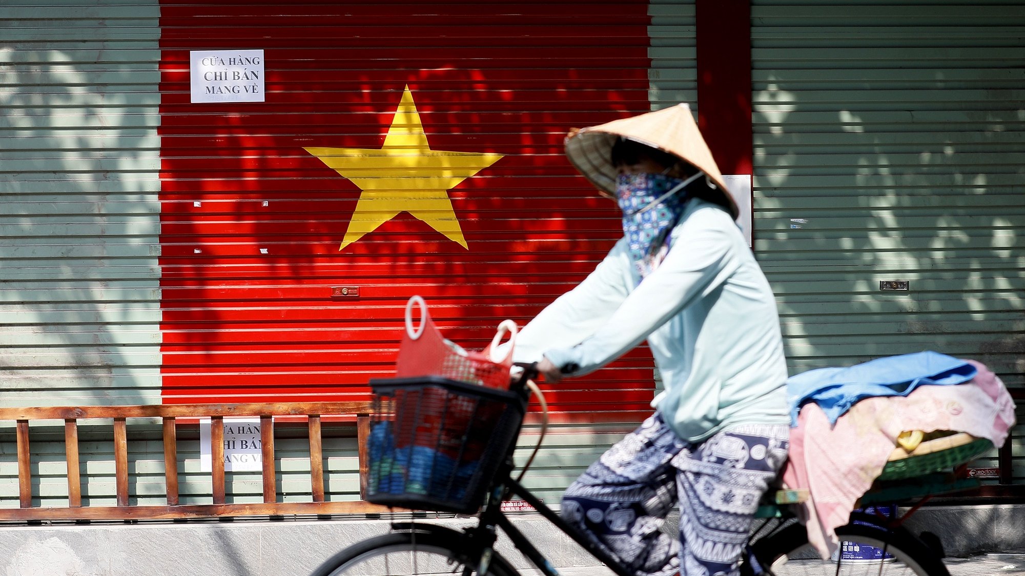 epa09352987 A woman wearing a face mask rides bicycle at a street in Hanoi, Vietnam, 19 July 2021. Vietnam tightened restrictions in 19 provinces, after nearly 6,000 new COVID-19 cases were reported in one day in the country.  EPA/LUONG THAI LINH