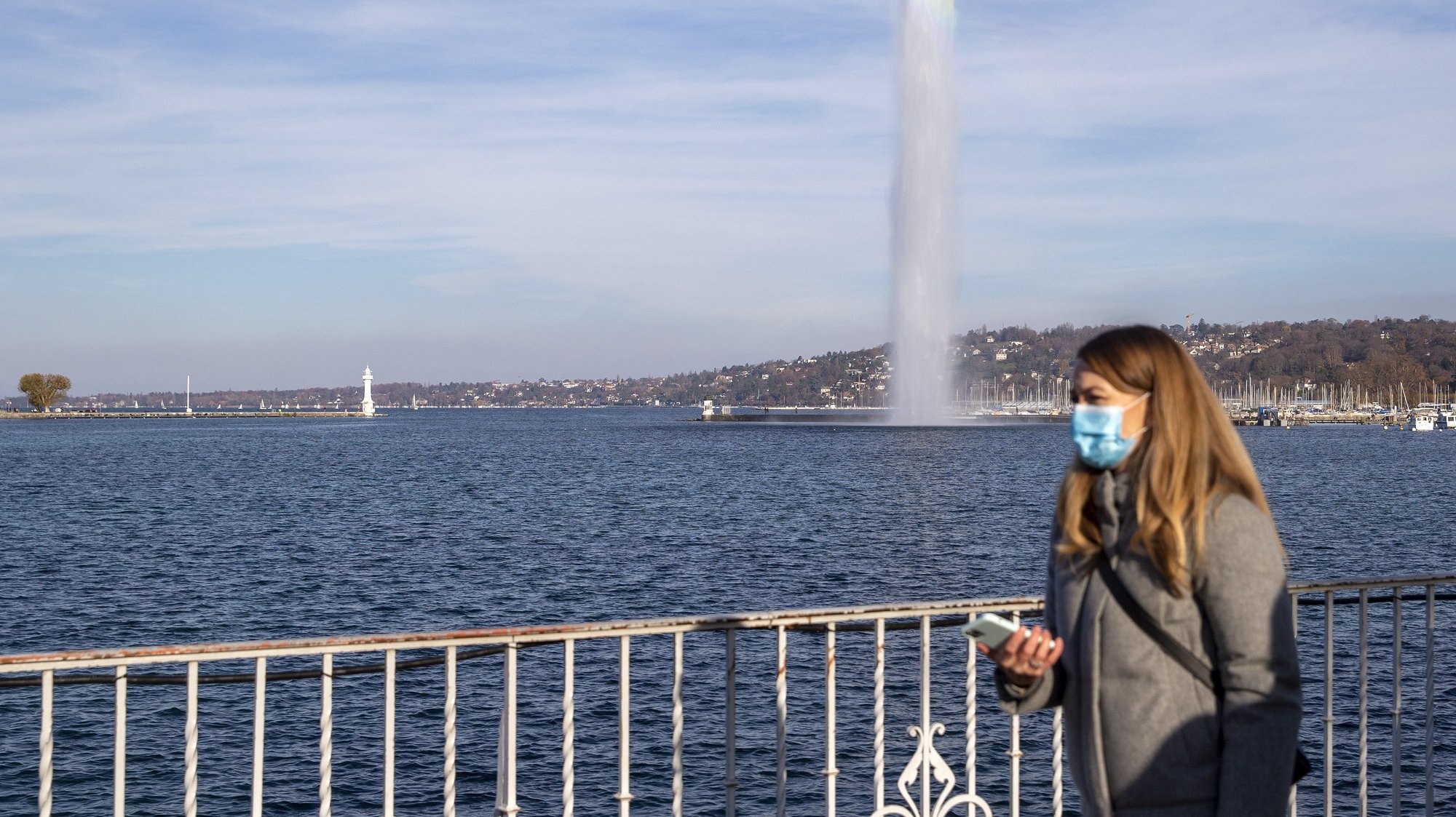 epa08833607 A woman wearing a face mask as precaution against the spread of the coronavirus COVID-19 walks past of the famous water fountain (Jet d&#039;eau), in Geneva, Switzerland, 21 November 2020. In Geneva, the Jet d&#039;eau resumed service on 21 November after was &#039;confined&#039; for nine days to remind the population of the health measures in connection with the second wave of coronavirus Covid-19 pandemic.  EPA/SALVATORE DI NOLFI