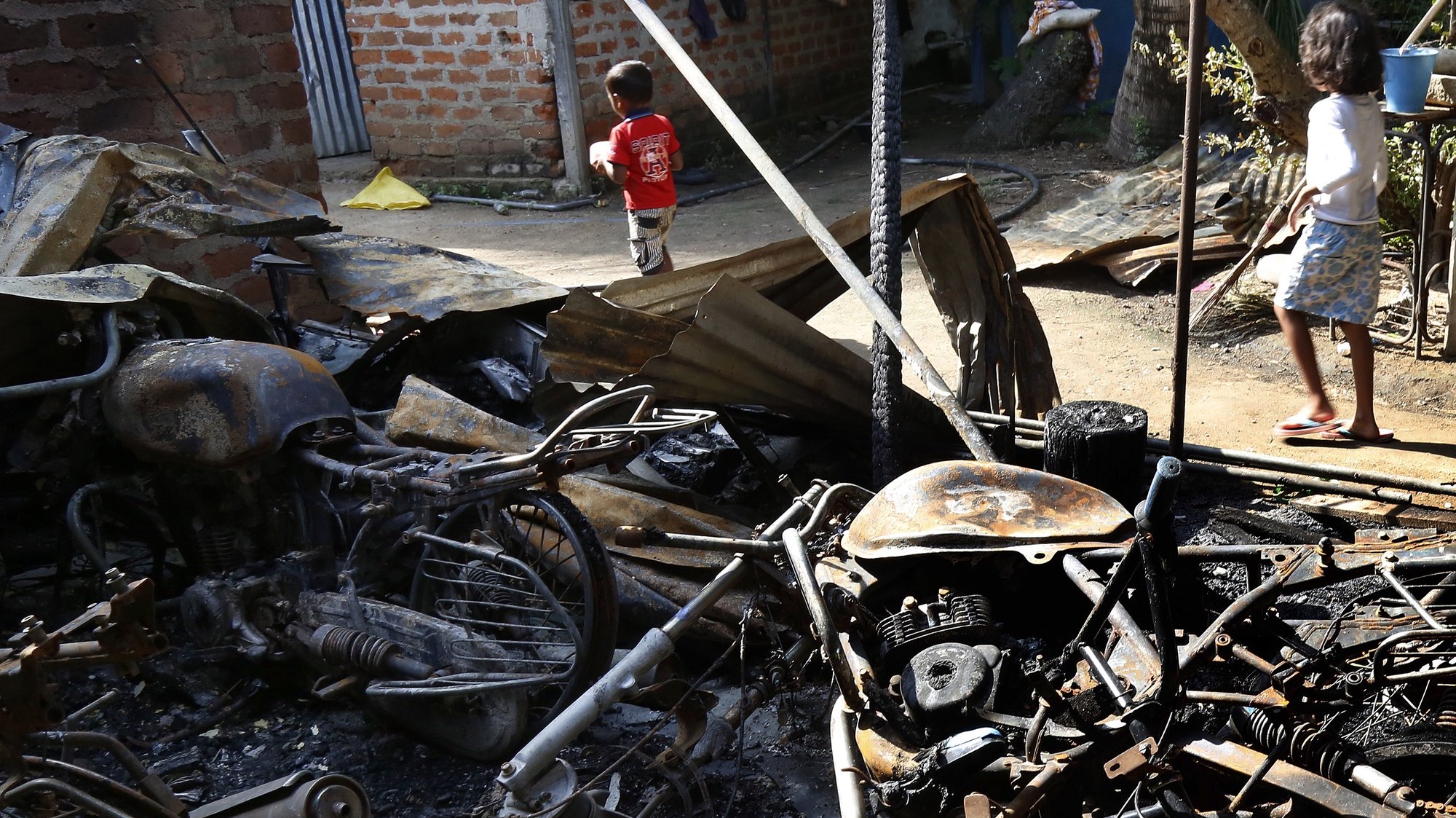epa07569790 Sri Lankan children pass near the burnt vehicles Hettipola area, 86 Kilometers from Colombo, Sri Lanka, 14 May 2019. According to news reports, Sri Lanka authorities imposed a nationwide overnight curfew after outbreak of communal violence and clashes in the aftermath of the deadly series of Easter bombings that killed over 300 people. One person was reportedly stabbed to death during the sectarian attacks, in which mosques and Muslim-owned shops were targeted.  EPA/M.A.PUSHPA KUMARA
