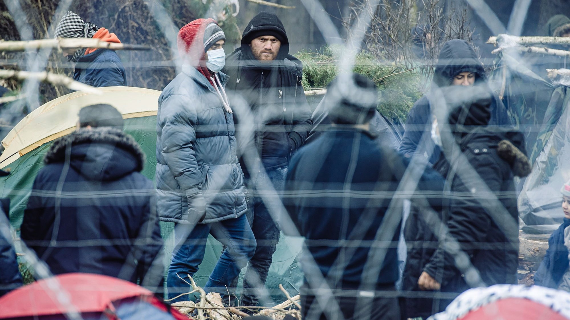 epa09581991 A handout photo made available by Territorial Defense Forces shows migrants behind the border fence in Belarus near the Polish-Belarusian border crossing in Kuznica, eastern Poland, 11 November 2021 (issued 14 November 2021). Poland has been struggling to stem the flow of Middle Eastern and African asylum-seekers, refugees and migrants crossing into Poland from Belarus. The Polish government says the migrants have been invited to Belarus by Alexander Lukashenko, the country&#039;s president, allegedly under the promise they will be able to live in the EU.  EPA/IREK DOROZANSKI HANDOUT POLAND OUT HANDOUT EDITORIAL USE ONLY/NO SALES