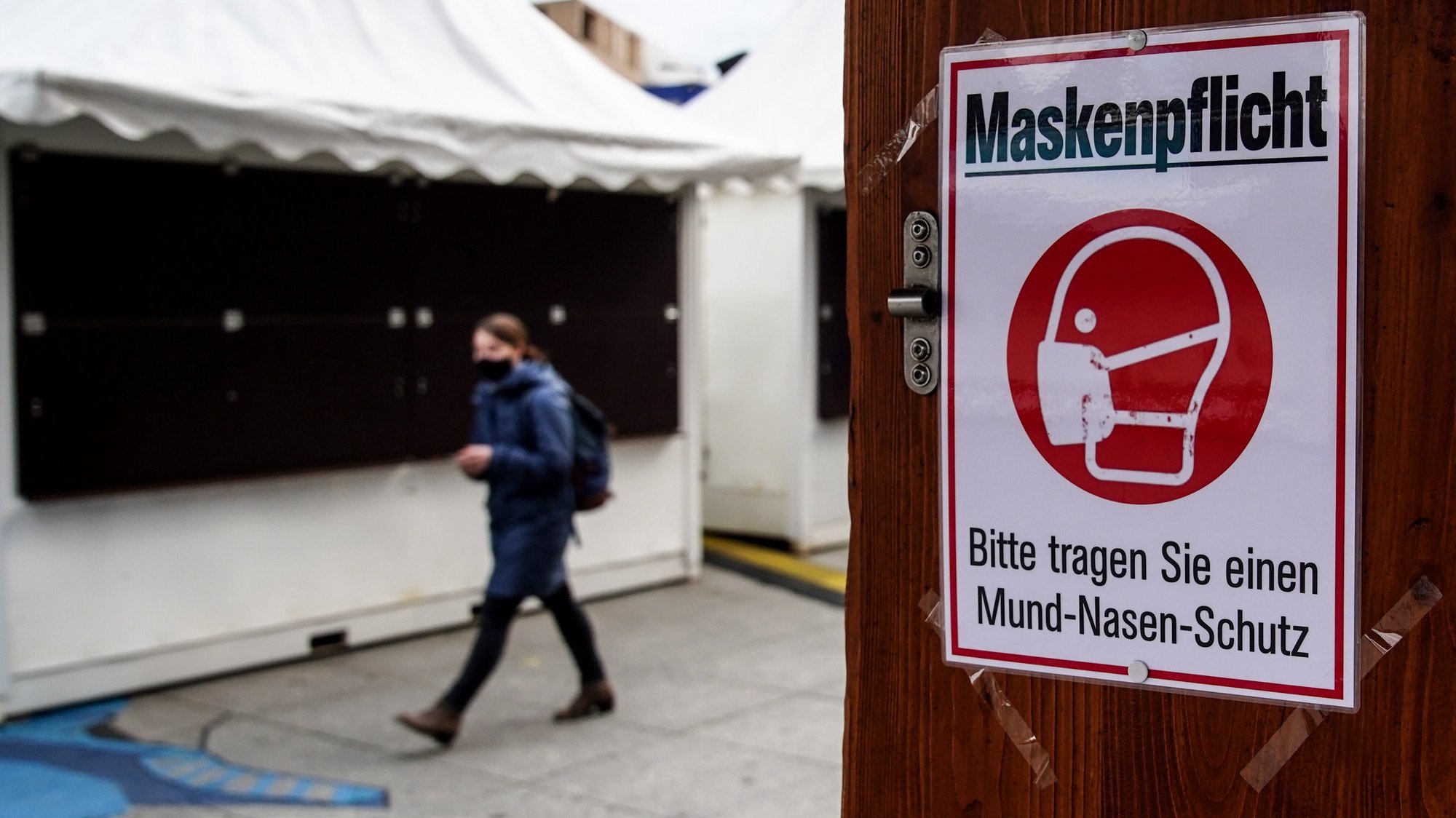 epa08824094 A woman walks next to a sign informing customers to wear face masks as she passes by a closed Christmas Market stall at Potsdamer Platz in Berlin, Germany, 16 November 2020. Effective from 02 November, Germany is on nationwide restrictions to prevent a further explosion in the number of corona infections, such as closing bars and restaurants for a month.  EPA/FILIP SINGER