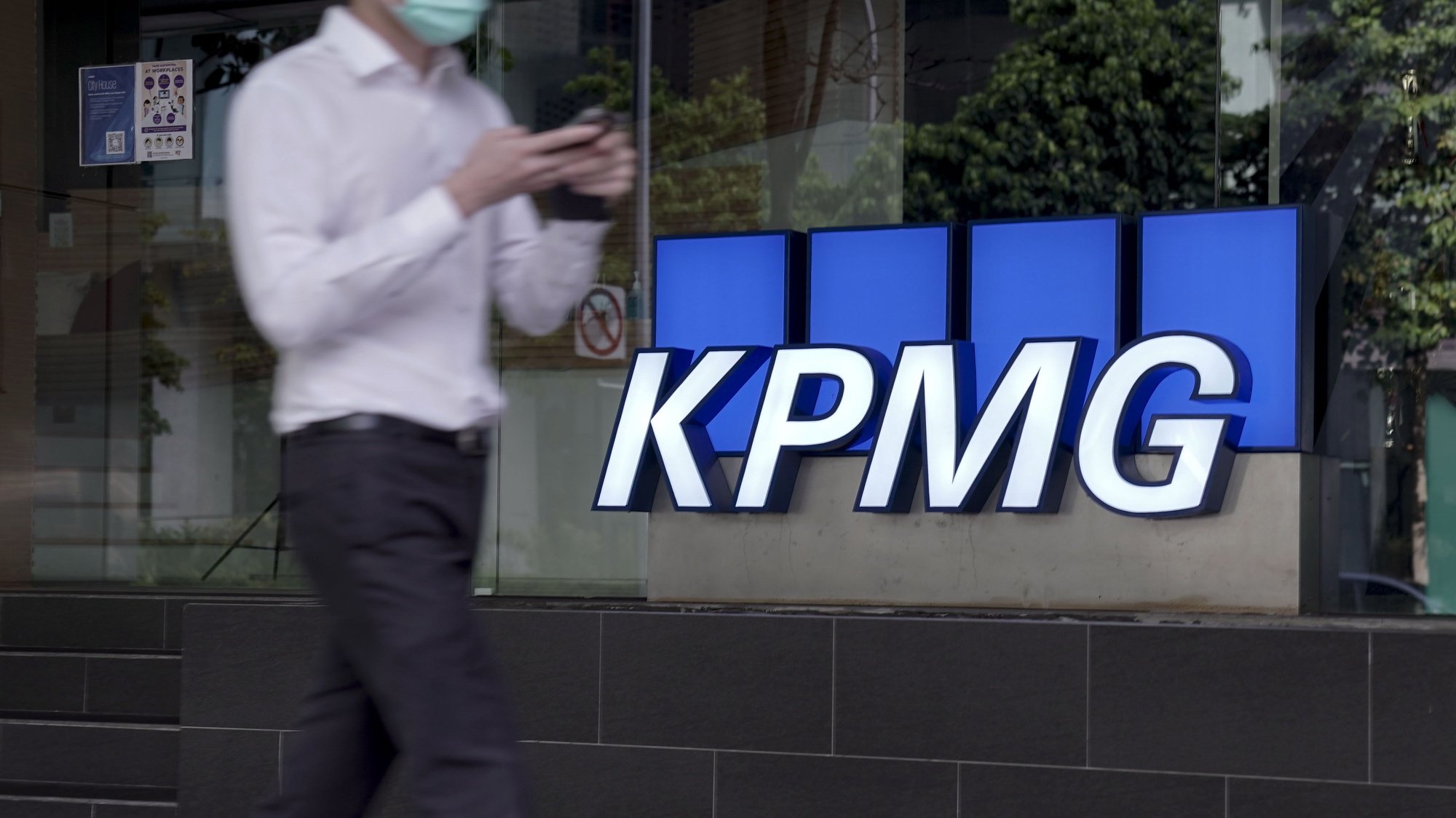 epa08777182 A man walks past the logo of auditing firm KPMG in the financial district in Singapore, 27 October 2020. The fallout of the global Covid-19 coronavirus pandemic has had a range of effects across workers from different sectors of the economy. As businesses gradually open up, economists are describing a &#039;K-shaped&#039; recovery caused by lower wage workers affected by health and safety regulations, while white collar workers remain largely unaffected due to the advent of telecommuting and work from home arrangements.  EPA/WALLACE WOON